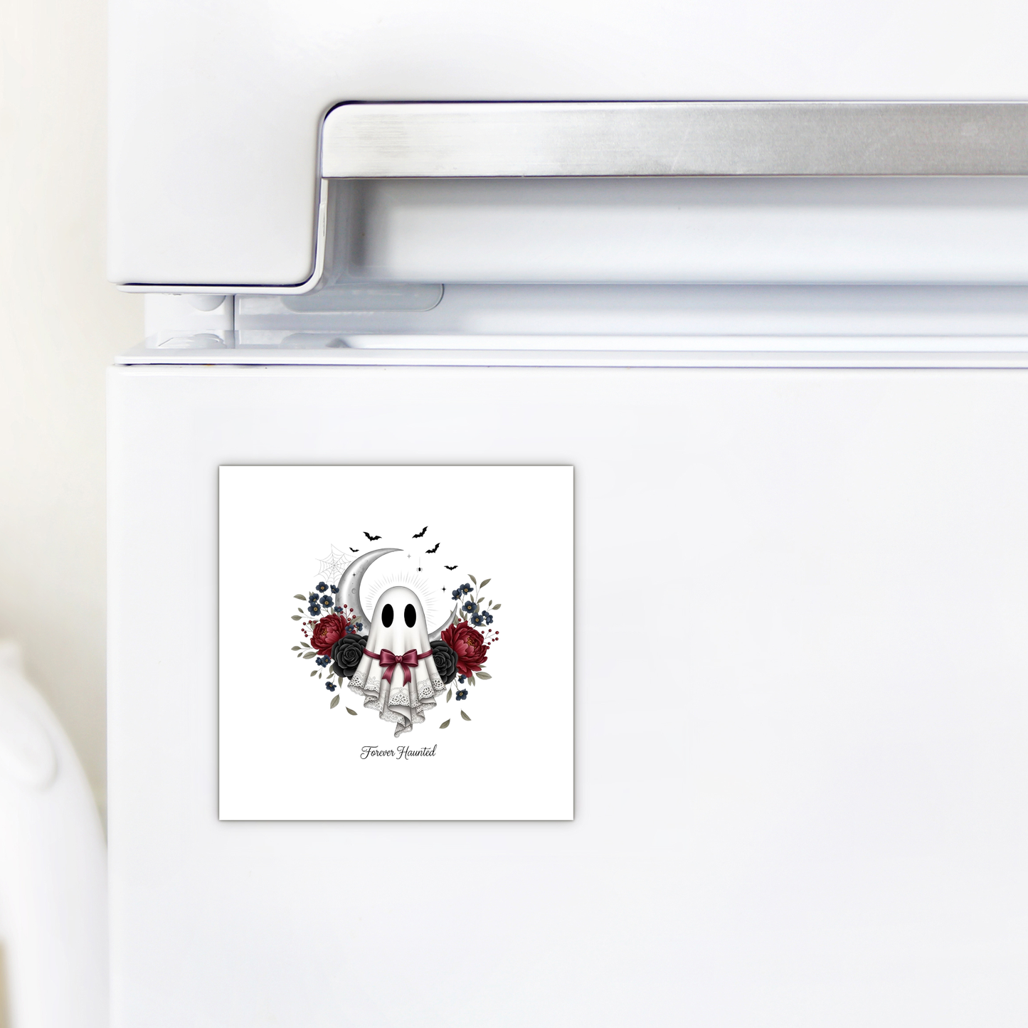 A white refrigerator adorned with the Forever Haunted Ghost Magnet by Mirabilia Boutique—a square, spooky magnet featuring a cartoon ghost, red and black flowers, a crescent moon, and the words "Haunt Yourself." Perfect as gothic Halloween décor or as a unique kitchen accent for Halloween.