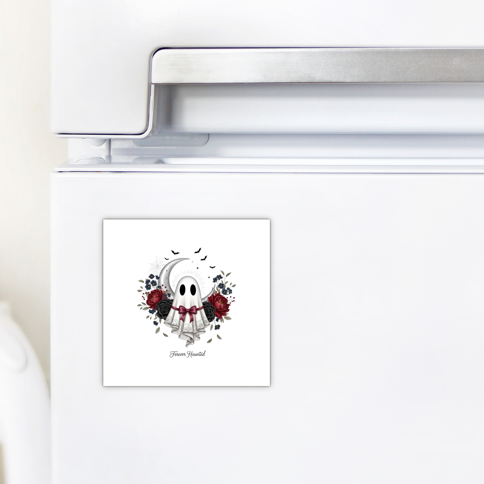 A white refrigerator adorned with the Forever Haunted Ghost Magnet by Mirabilia Boutique—a square, spooky magnet featuring a cartoon ghost, red and black flowers, a crescent moon, and the words "Haunt Yourself." Perfect as gothic Halloween décor or as a unique kitchen accent for Halloween.