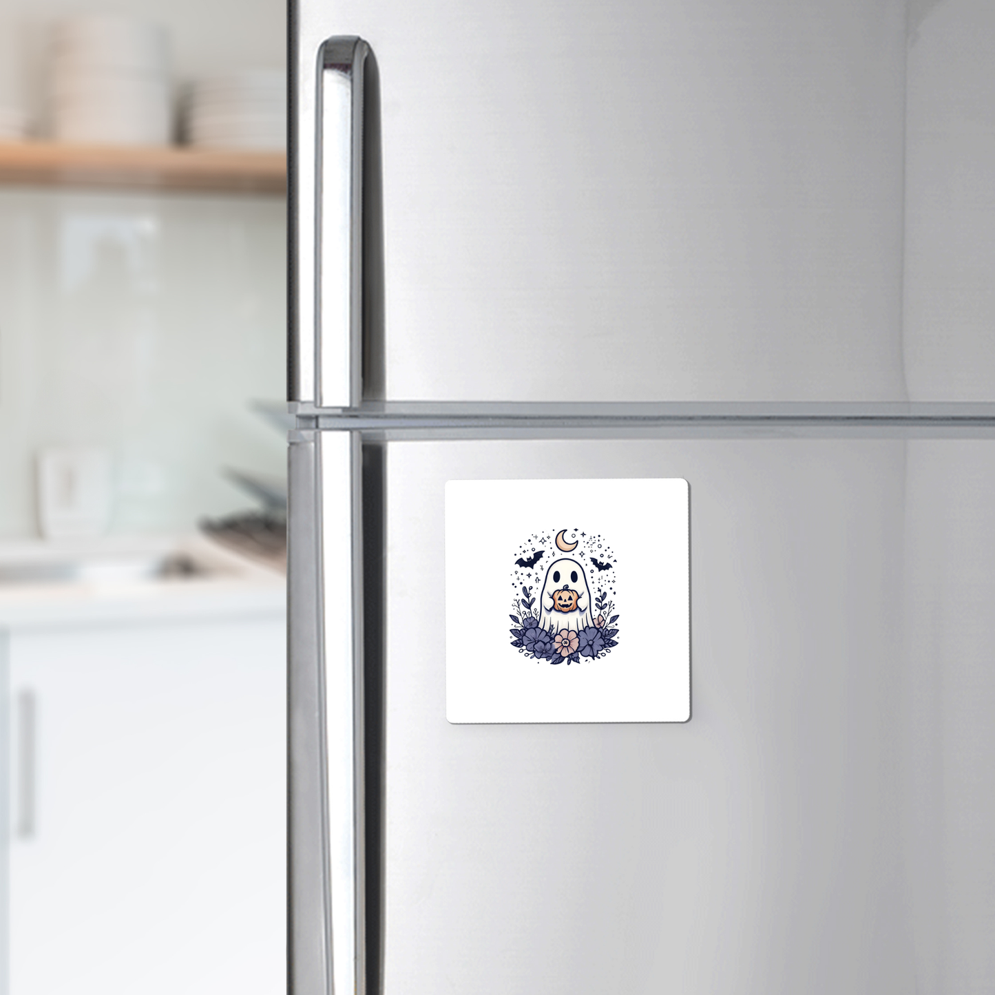 A silver refrigerator features a square white magnet displaying an adorable owl, moon, and stars illustration, bringing charm to your kitchen. For a festive touch this season, pair it with the Cute Ghost Pumpkin Magnet from Mirabilia Boutique—its whimsical Halloween design complements your other decorative accents beautifully. Kitchen shelves and dishes can be seen in the background.