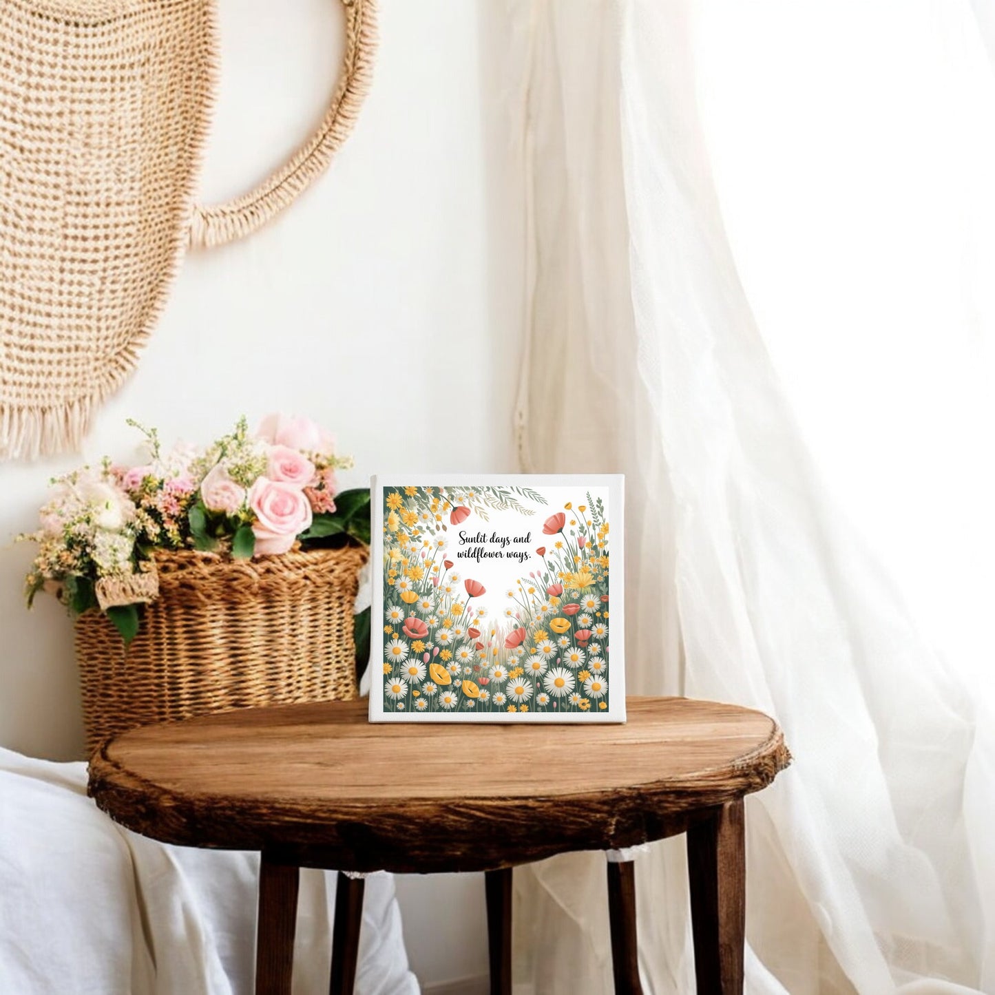 A Sunlit Days and Wildflower Ways Canvas by Mirabilia Boutique brings cottagecore charm to a cozy room, with a wooden table, floral card, wicker basket of pink flowers, and soft light enhancing the tranquil vibe.