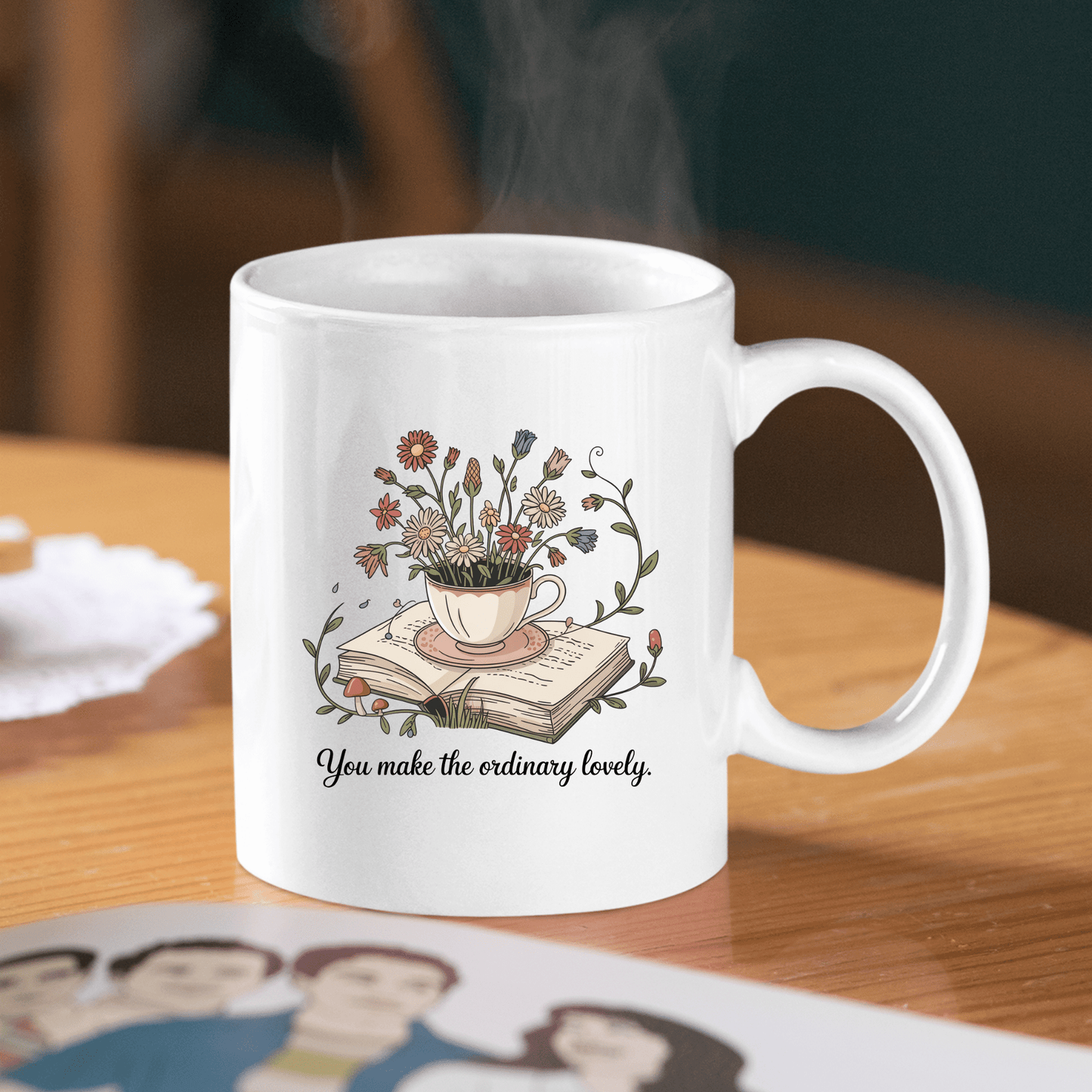 The You Make The Ordinary Lovely | Floral Teacup Mug by Mirabilia Boutique is a white ceramic mug featuring wildflowers in a teacup on an open book with the phrase “You make the ordinary lovely”—a delightful gift for book lovers.