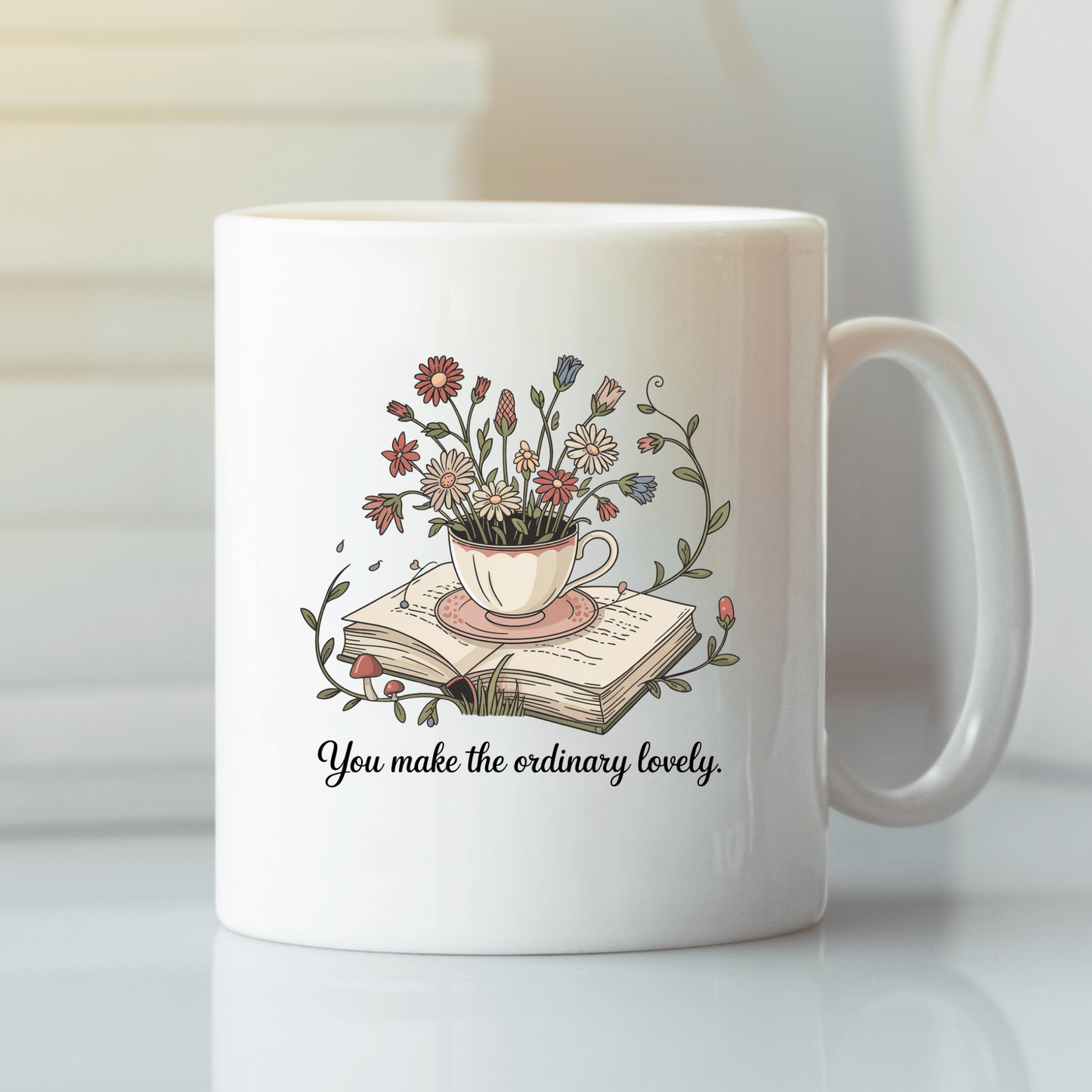 The “You Make The Ordinary Lovely | Floral Teacup Mug” by Mirabilia Boutique features wildflowers in a teacup atop an open book, plus the quote "You make the ordinary lovely"—a charming gift for book lovers.