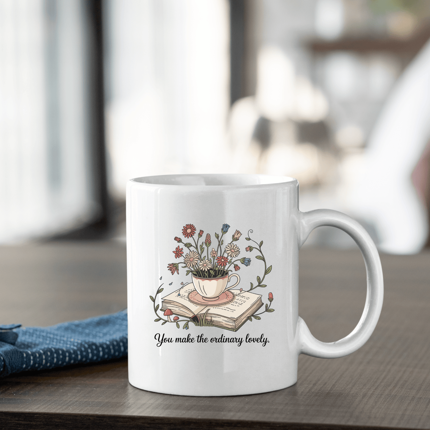 The "You Make The Ordinary Lovely | Floral Teacup Mug" from Mirabilia Boutique features a floral teacup design with wildflowers and uplifting text—a charming ceramic mug and a perfect gift for book lovers.