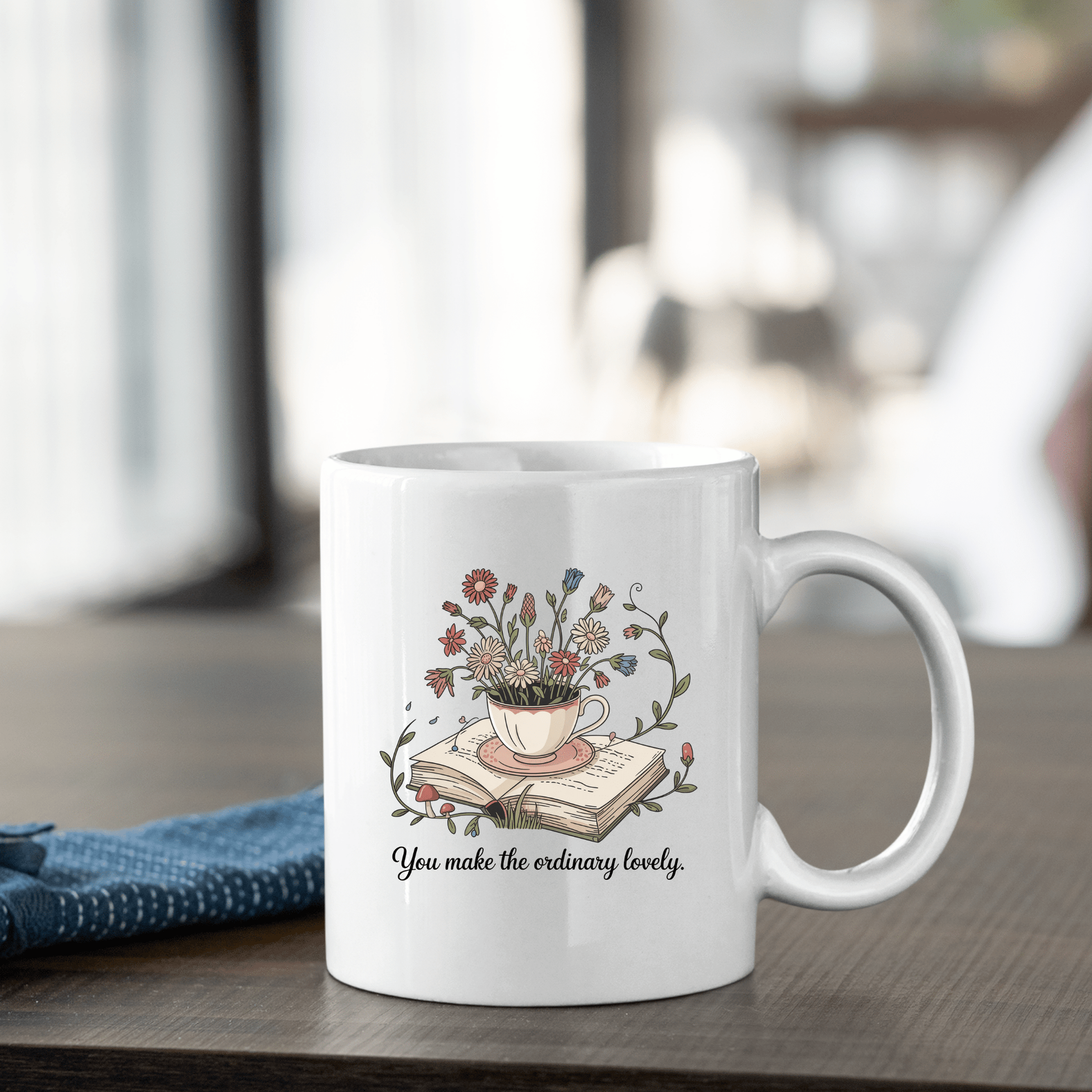 The "You Make The Ordinary Lovely | Floral Teacup Mug" from Mirabilia Boutique features a floral teacup design with wildflowers and uplifting text—a charming ceramic mug and a perfect gift for book lovers.