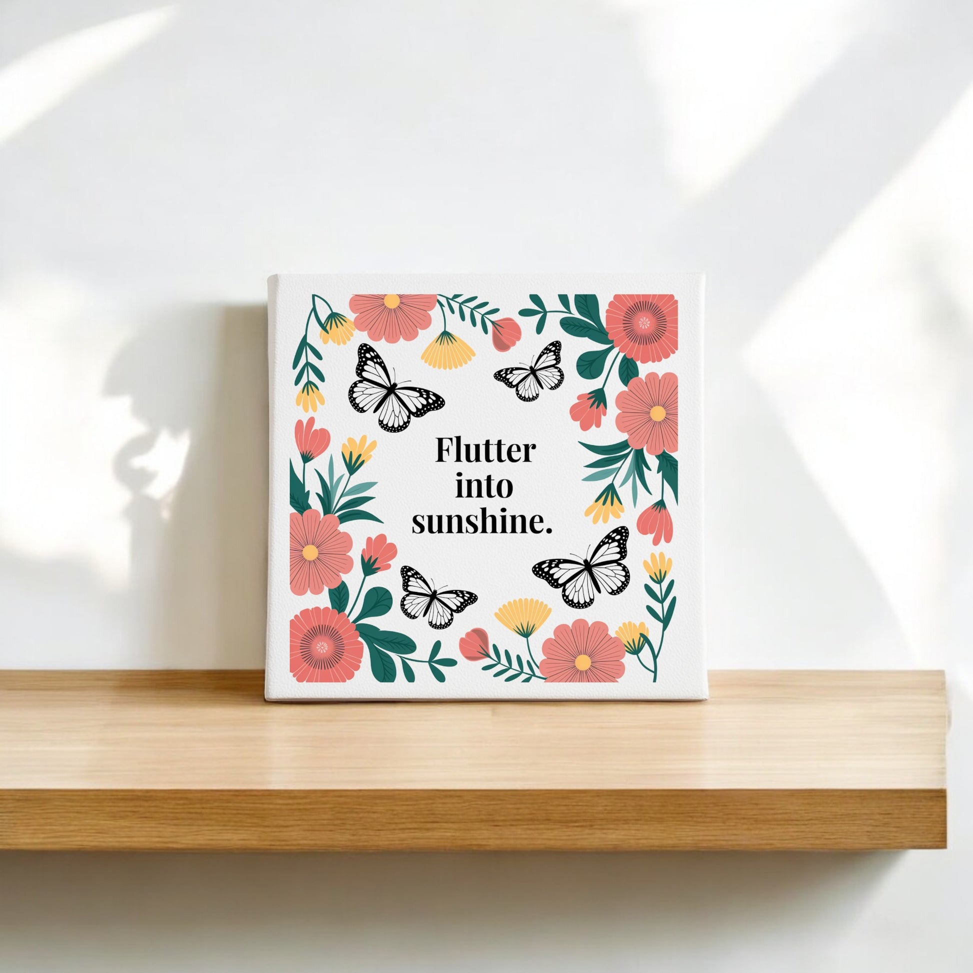 The Mirabilia Boutique "Flutter into Sunshine Canvas – Butterflies & Floral Joy" features illustrated butterflies and colorful flowers around the quote, creating uplifting wall art perfect for display on a shelf or white wall.
