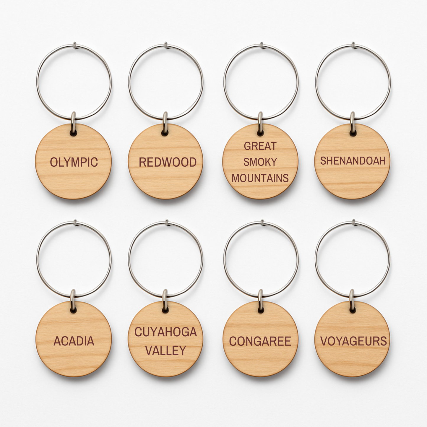 Eight Forest And Fog Wine Charms by Mirabilia Boutique are arranged in two rows, each featuring a U.S. national park’s name—perfect for nature lovers who admire woodland landscapes like Olympic, Redwood, Shenandoah, and more.