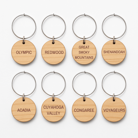 Eight Forest And Fog Wine Charms by Mirabilia Boutique are arranged in two rows, each featuring a U.S. national park’s name—perfect for nature lovers who admire woodland landscapes like Olympic, Redwood, Shenandoah, and more.