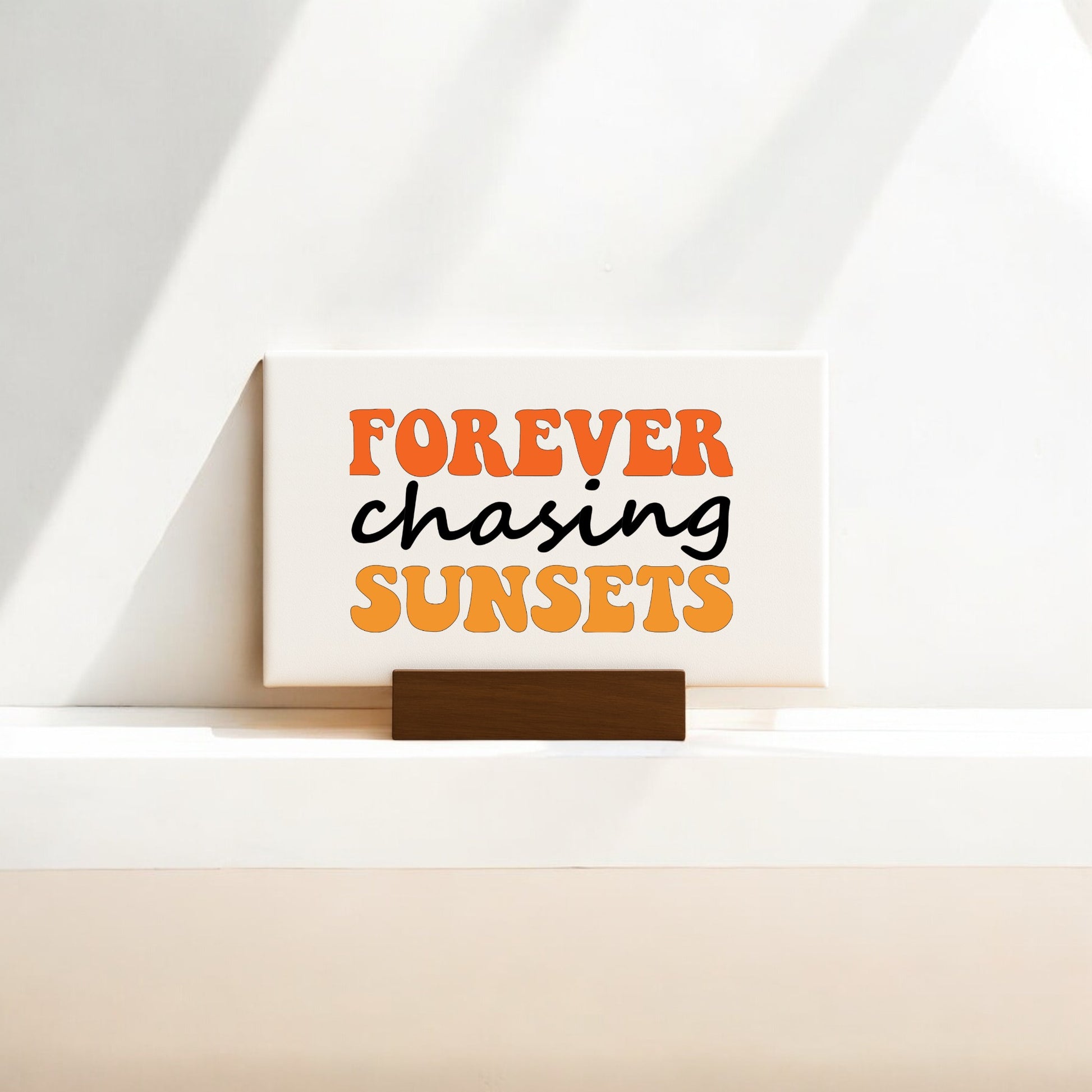 The Mirabilia Boutique "Forever Chasing Sunsets Canvas – Retro Mini Sign" features bold orange and black text on a bright background with sunlit shadows—a charming decor piece for sunset lovers and mini canvas art fans.