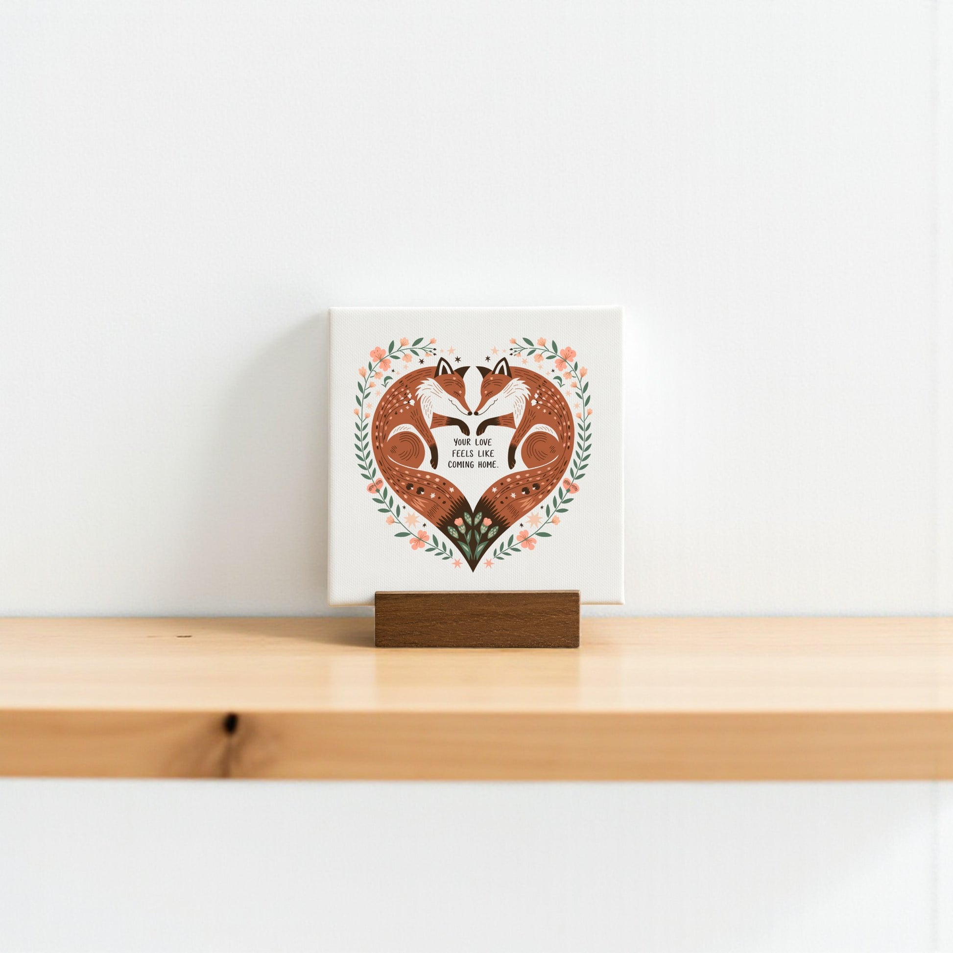 The Fox Love Mini Canvas by Mirabilia Boutique features two foxes forming a heart with their tails and the quote “Your Love Feels Like Home.” Perfect for adding rustic charm and romance to any shelf or woodland-themed décor.