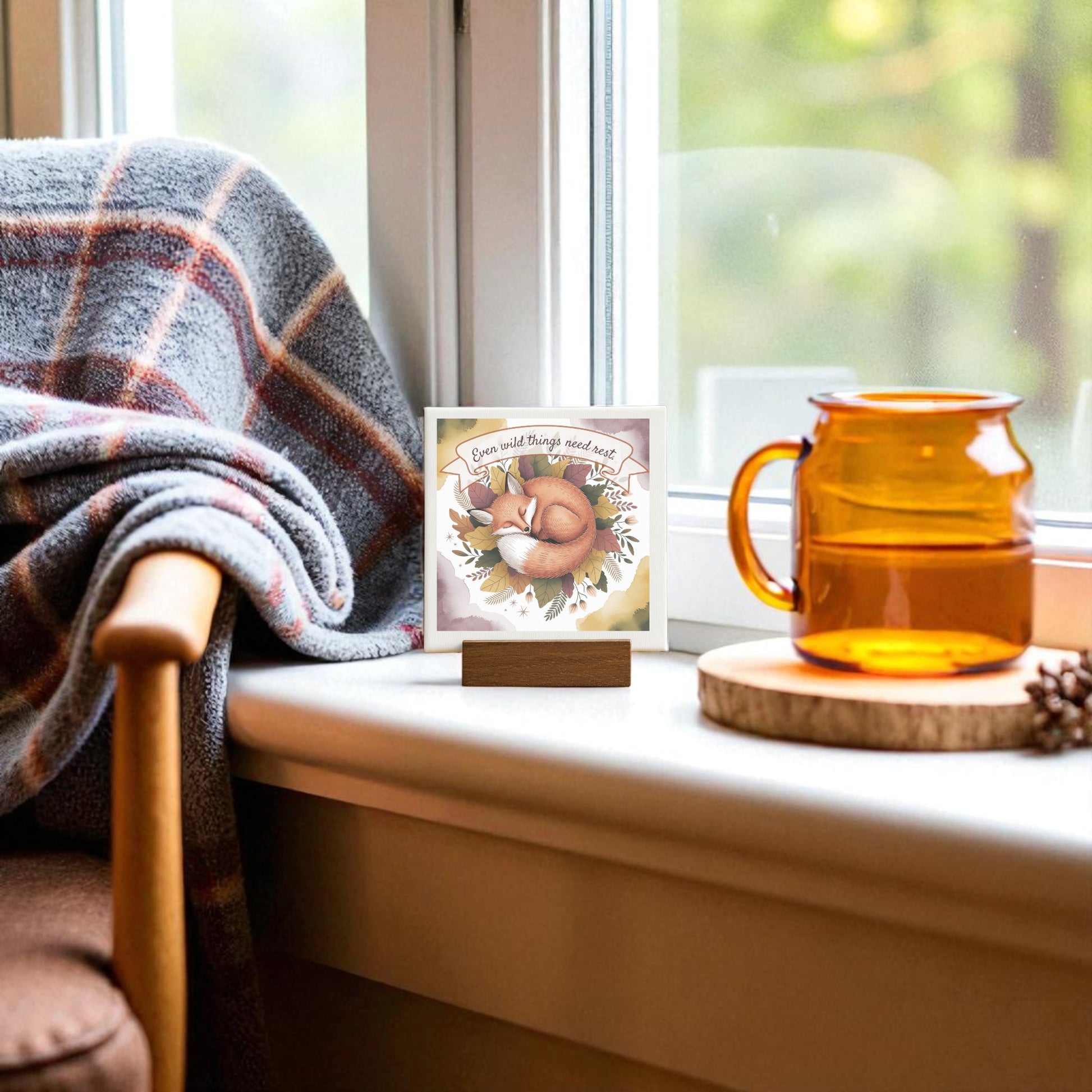 A cozy window scene with a plaid blanket, amber glass mug, and Mirabilia Boutique’s Fox Nature Art Print—featuring the quote “Even Wild Things Need Rest”—makes perfect woodland home décor.