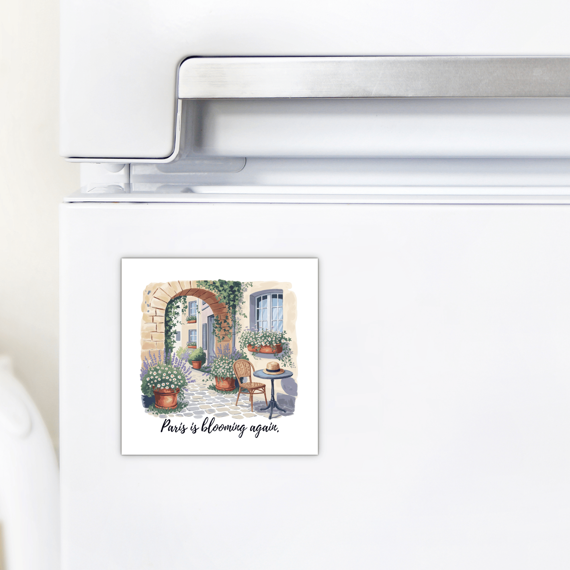 The Mirabilia Boutique Paris Is Blooming Again – Spring Courtyard Magnet features a charming Parisian courtyard scene with flowers, plants, table, and chairs, plus the text "Paris is blooming again"—perfect for spring kitchen décor.