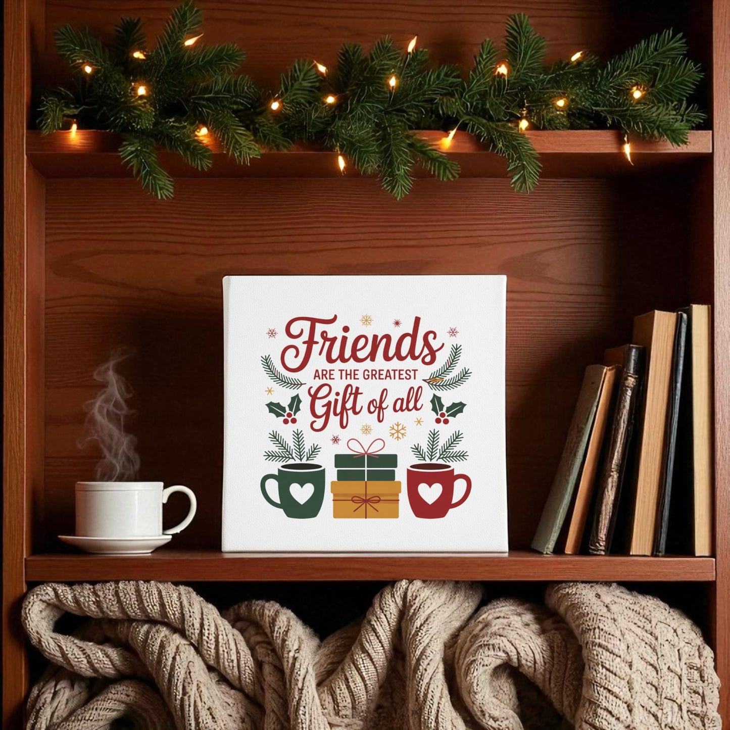 A festive shelf features Mirabilia Boutique’s Friends Gift Canvas (8x8 Holiday Wall Art) with two mugs, a gift box, pine garland, books, and cozy knit blankets—the perfect Christmas gift for friends.