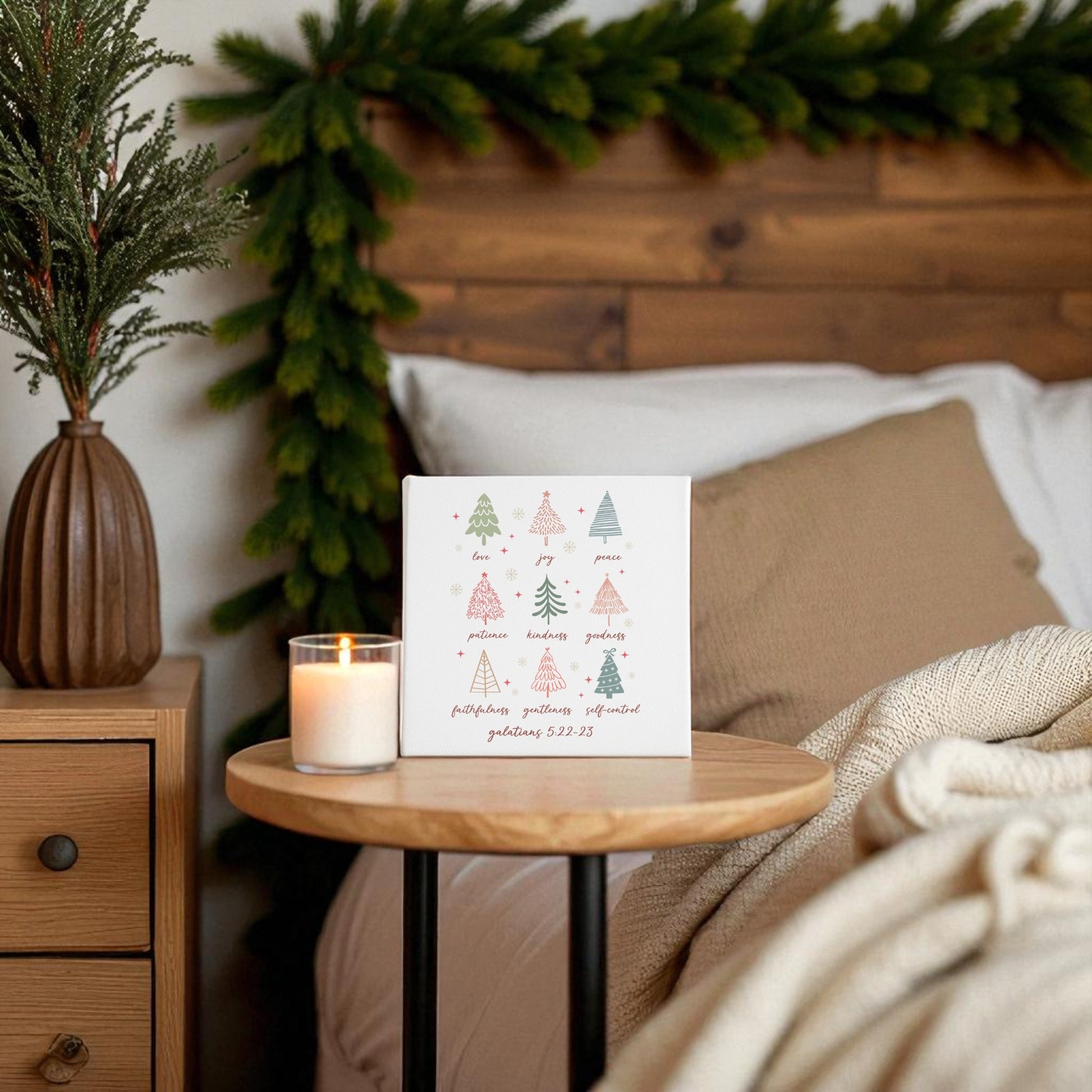 A cozy bedroom features Mirabilia Boutique's "Fruits of the Spirit" Christian Christmas Canvas, lit candle on a bedside table, and evergreen garland. Faith-filled decor and neutral bedding create a festive, warm holiday atmosphere.