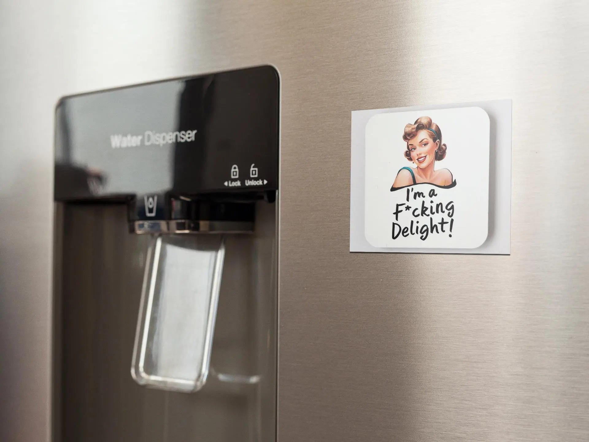 A close-up image of a water dispenser on a stainless steel refrigerator, next to a snarky retro magnet from Mirabilia Boutique featuring a cartoon of a woman. The humorous fridge magnet reads, "I'm a Fucking Delight!