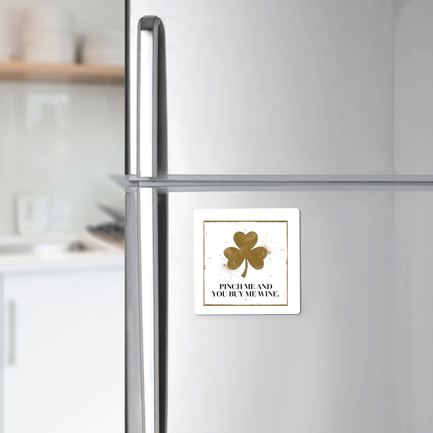 A silver refrigerator displays the Mirabilia Boutique "Pinch Me and You Buy Me Wine Magnet," a square magnet with a gold shamrock—perfect St. Patrick’s Day gift for wine lovers. Kitchen shelves and dishes blur softly in the background.