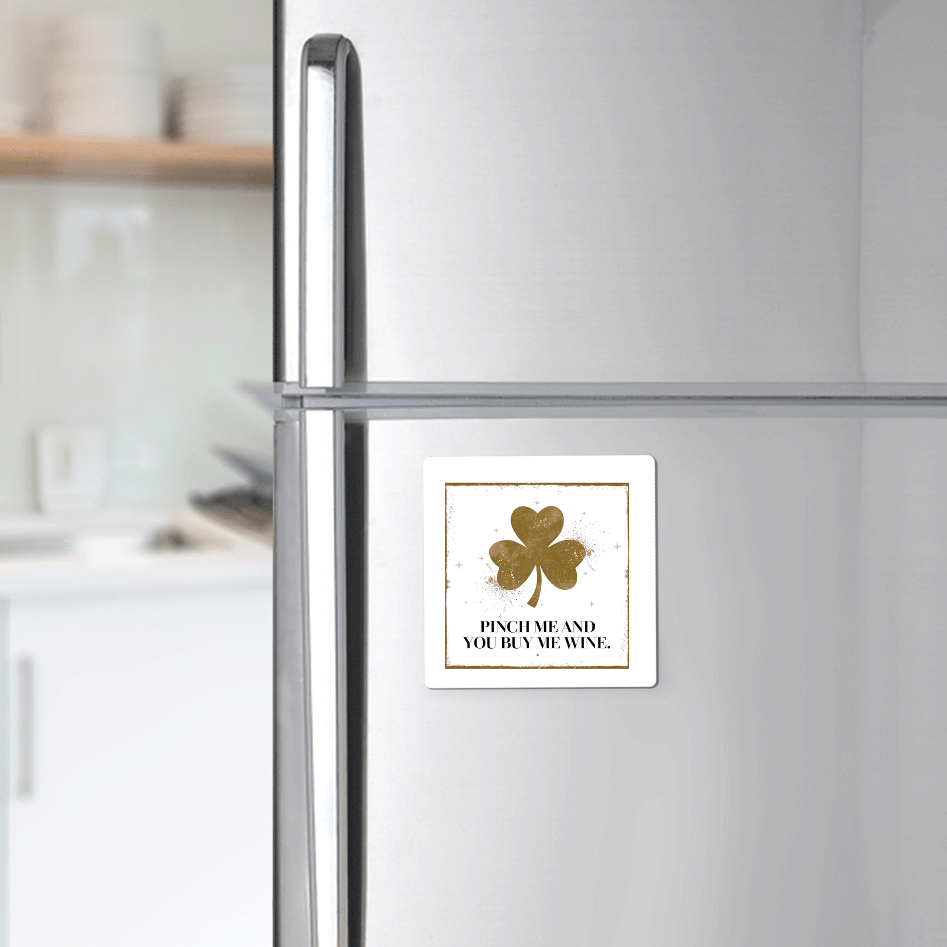 A silver refrigerator displays the Mirabilia Boutique "Pinch Me and You Buy Me Wine Magnet," a square magnet with a gold shamrock—perfect St. Patrick’s Day gift for wine lovers. Kitchen shelves and dishes blur softly in the background.