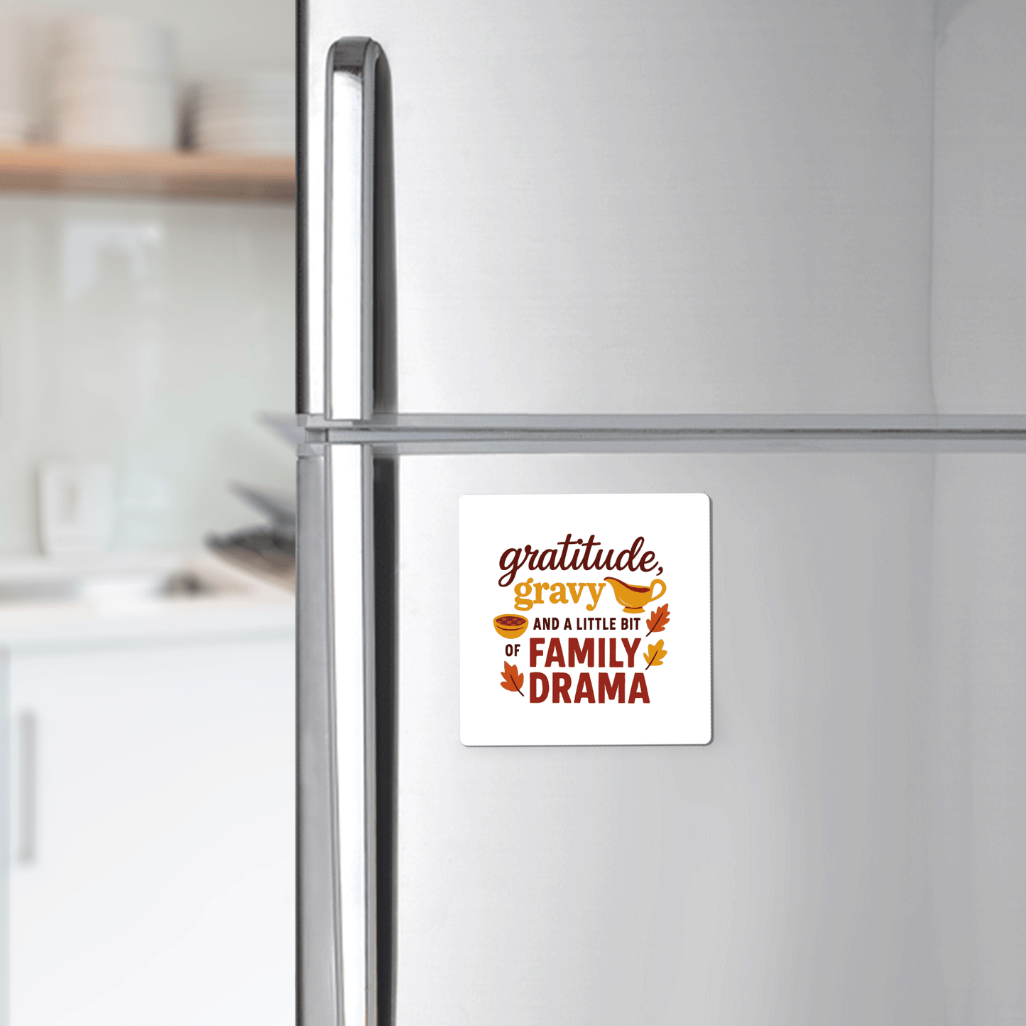 A modern kitchen features a refrigerator decorated with Mirabilia Boutique’s Gratitude Gravy & Family Drama Magnet, a funny fall decor piece that reads, “Gratitude, gravy, and a little bit of family drama,” surrounded by autumn leaves.