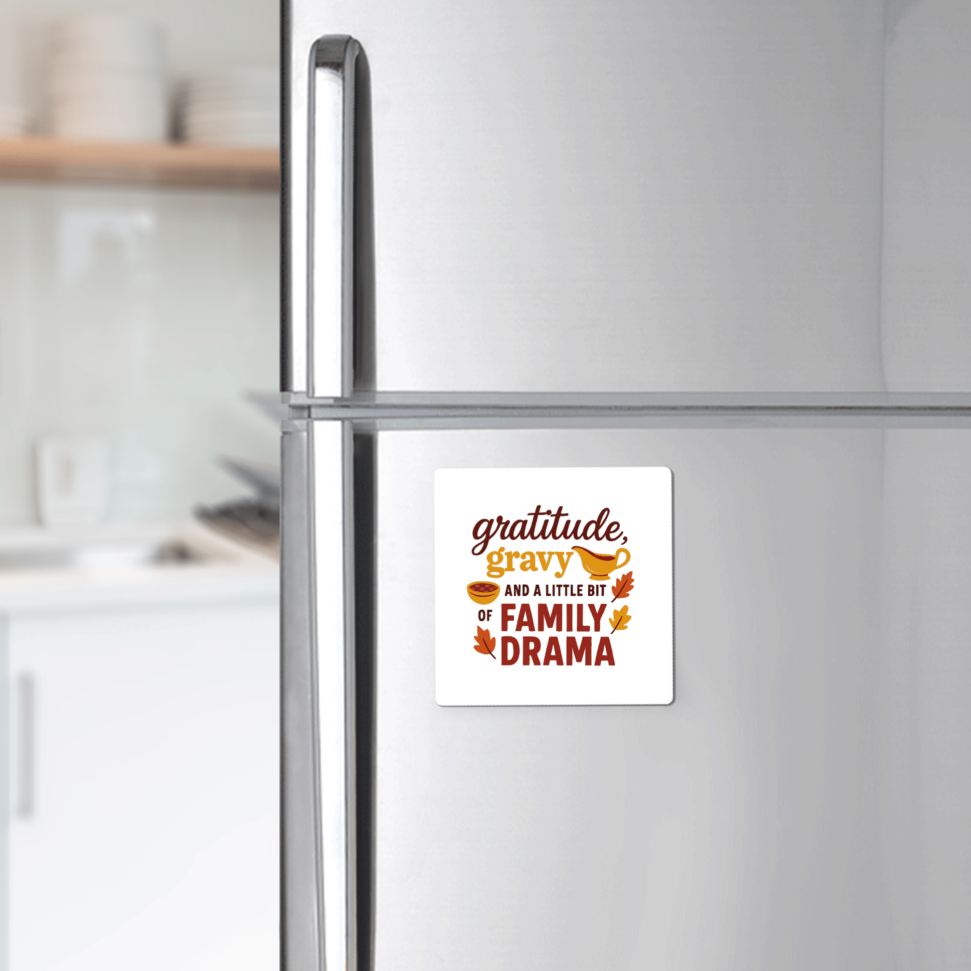 A modern kitchen features a refrigerator decorated with Mirabilia Boutique’s Gratitude Gravy & Family Drama Magnet, a funny fall decor piece that reads, “Gratitude, gravy, and a little bit of family drama,” surrounded by autumn leaves.
