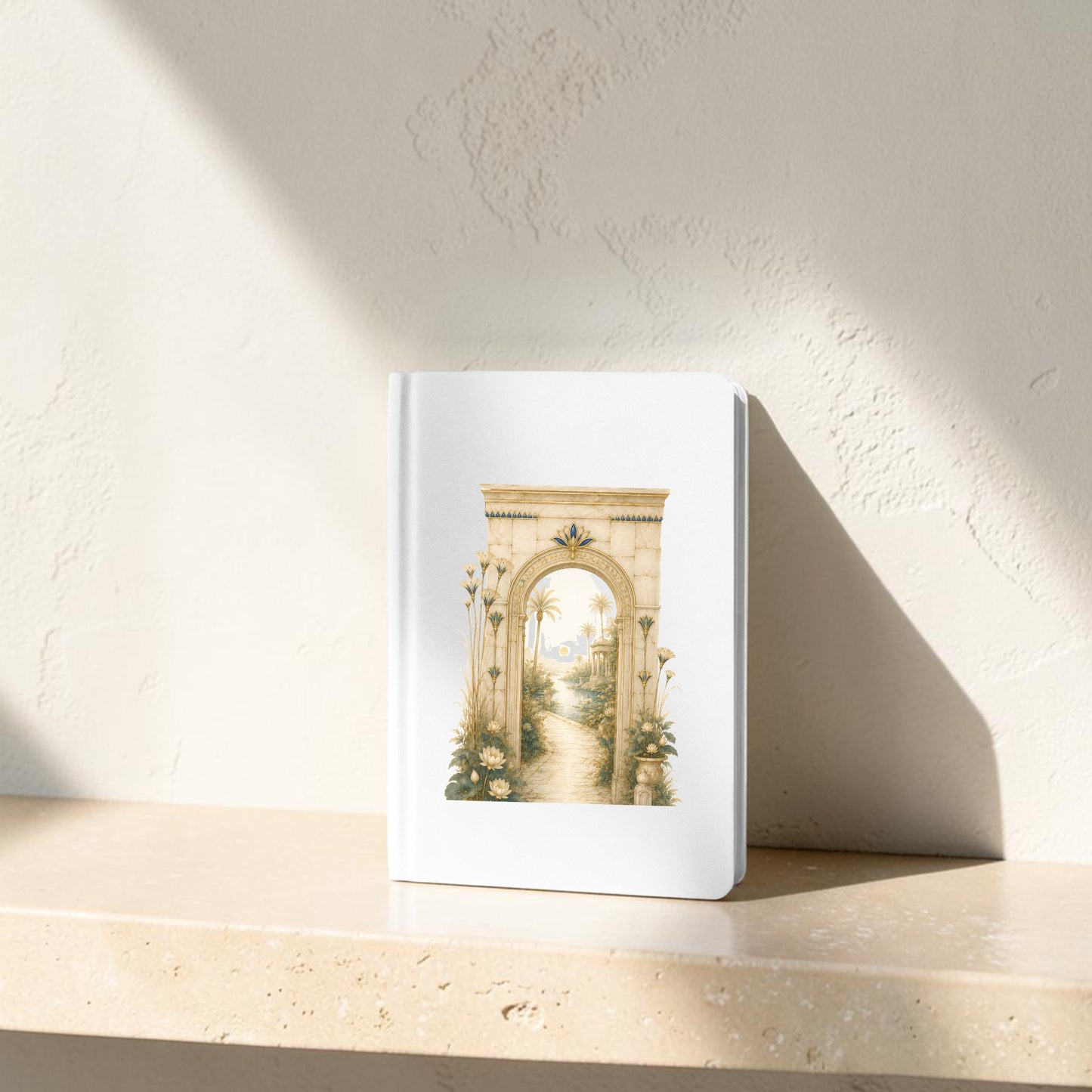 The Garden Path Journal | Ancient Egyptian Inspired Notebook from Mirabilia Boutique, featuring an illustration of an ancient stone archway and a winding path, rests on a beige stone shelf against a textured off-white wall with sunlight casting gentle shadows.