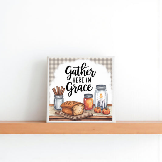 The Gather Here in Grace Canvas by Mirabilia Boutique features bread, candles, pumpkins, and cinnamon sticks on a wooden shelf with the quote above—an 8x8 farmhouse kitchen sign perfect for wall art or decor.