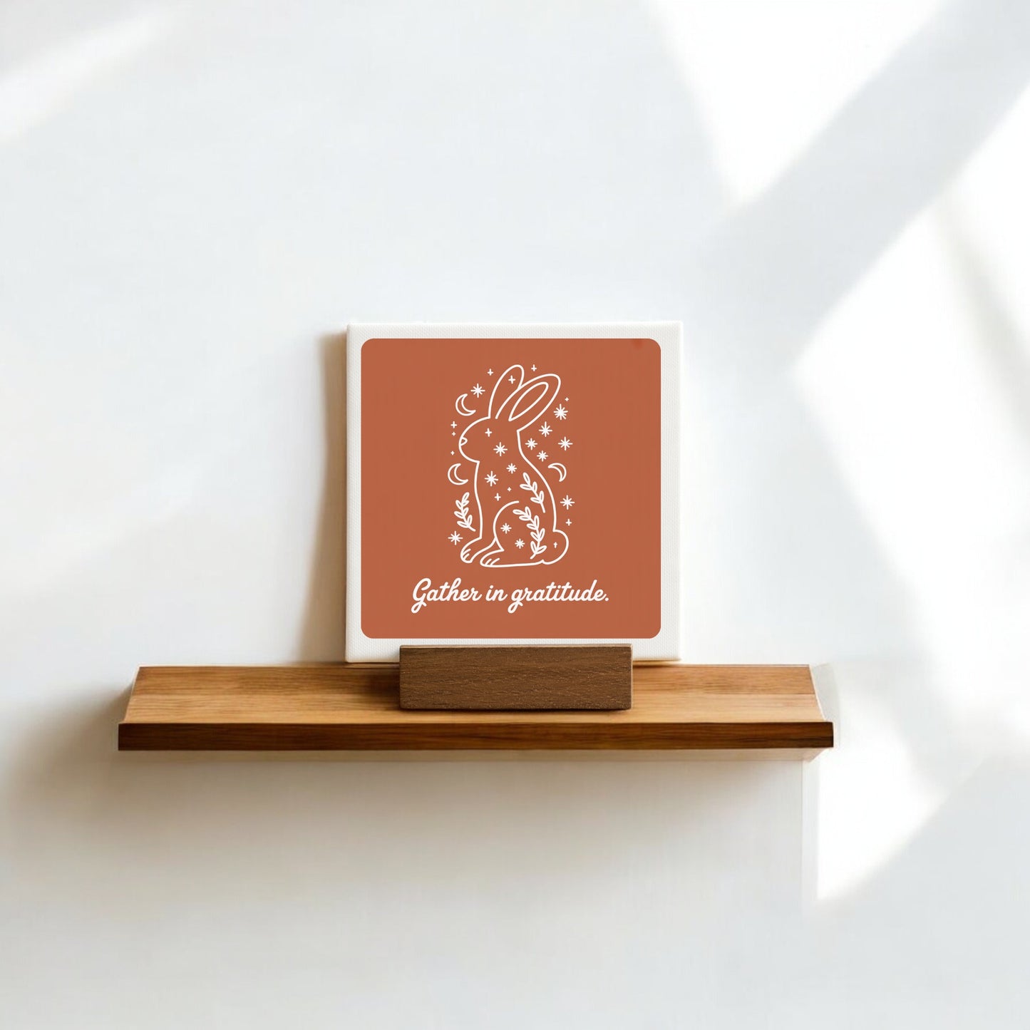 The Mirabilia Boutique "Gather in Gratitude" Mini Canvas Sign – 4x4 Bunny features a white bunny with stars, plants, and the moon—ideal as gratitude decor or shelf art against a white wall.