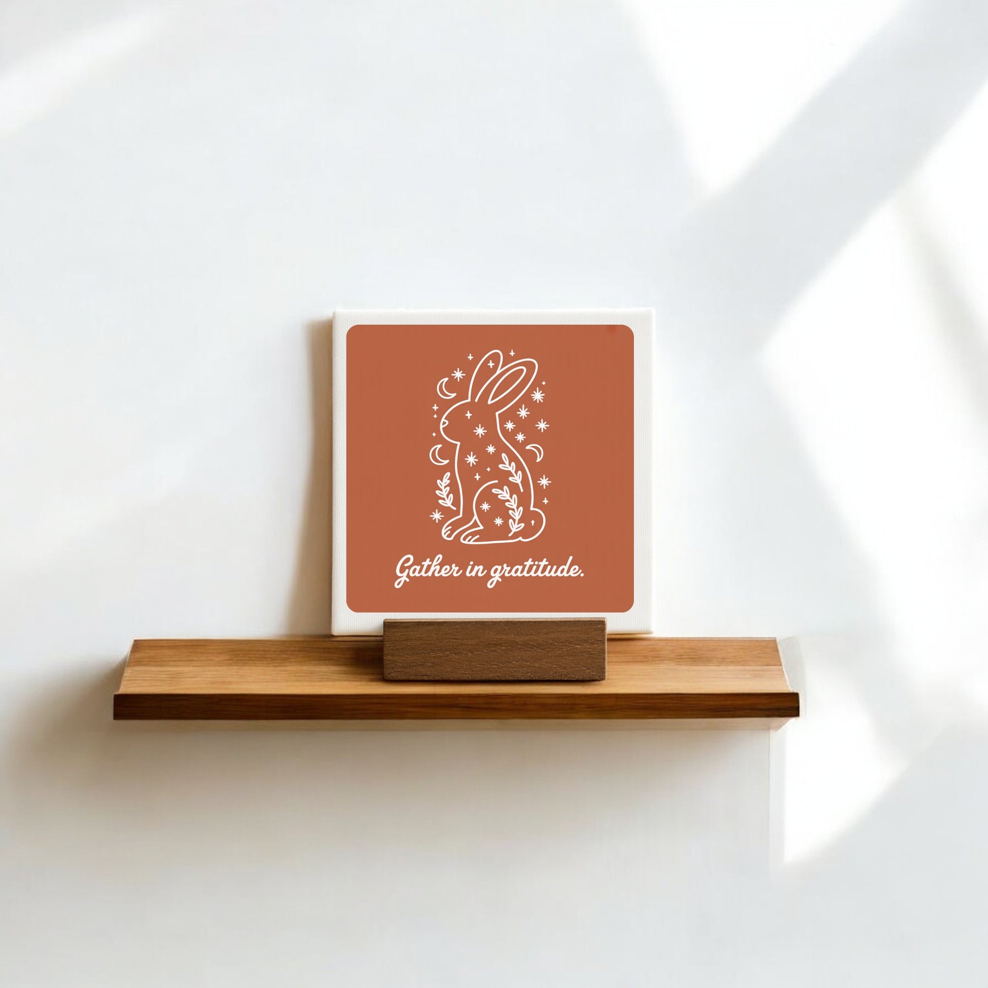 The Mirabilia Boutique "Gather in Gratitude" Mini Canvas Sign – 4x4 Bunny features a white bunny with stars, plants, and the moon—ideal as gratitude decor or shelf art against a white wall.