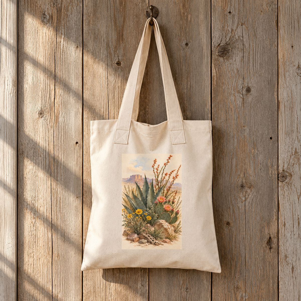 The Gathered From the Desert Tote Bag | Sage & Stone by Mirabilia Boutique features printed desert plants and agave artwork on beige canvas, shown hanging with sunlight casting diagonal shadows.