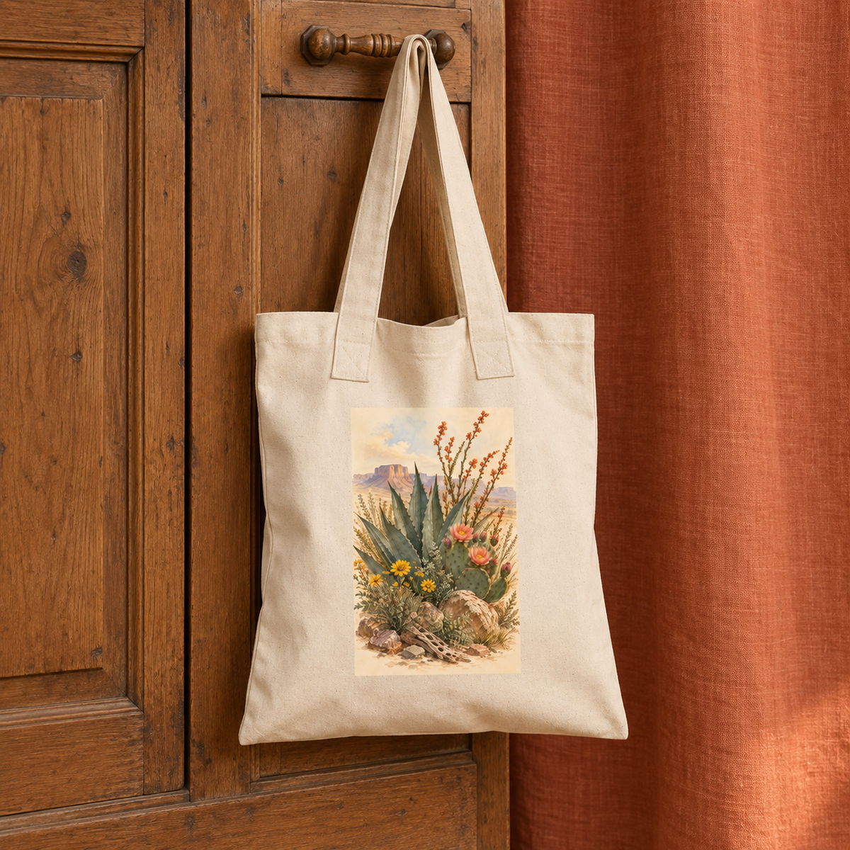 The Gathered From the Desert Tote Bag | Sage & Stone by Mirabilia Boutique, featuring agave art in beige, hangs on a wooden cabinet door beside a rust-colored curtain.