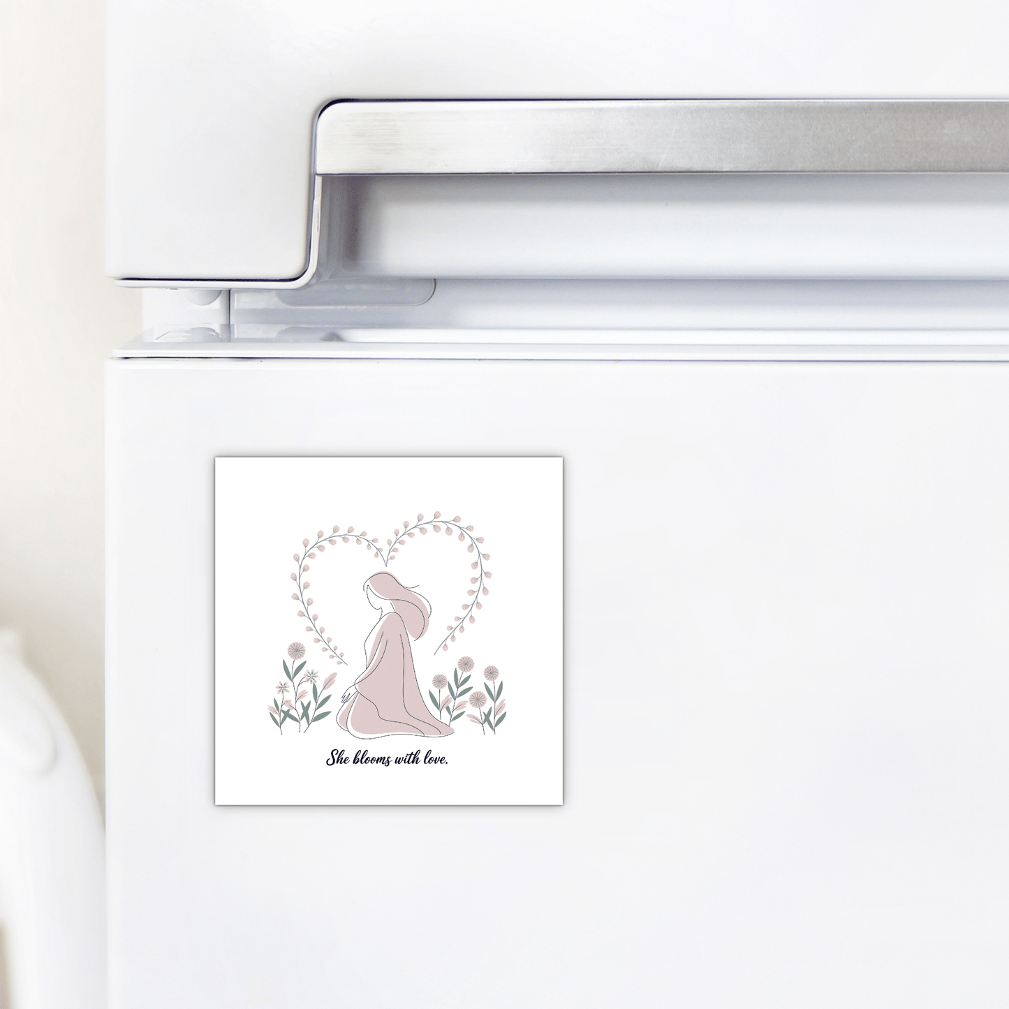 The Mirabilia Boutique She Blooms with Love Magnet – Gentle Floral Mom Gift, shown on a white fridge, depicts a woman in a hat within a heart of flowers and branches—an ideal decorative piece or special motherhood gift.