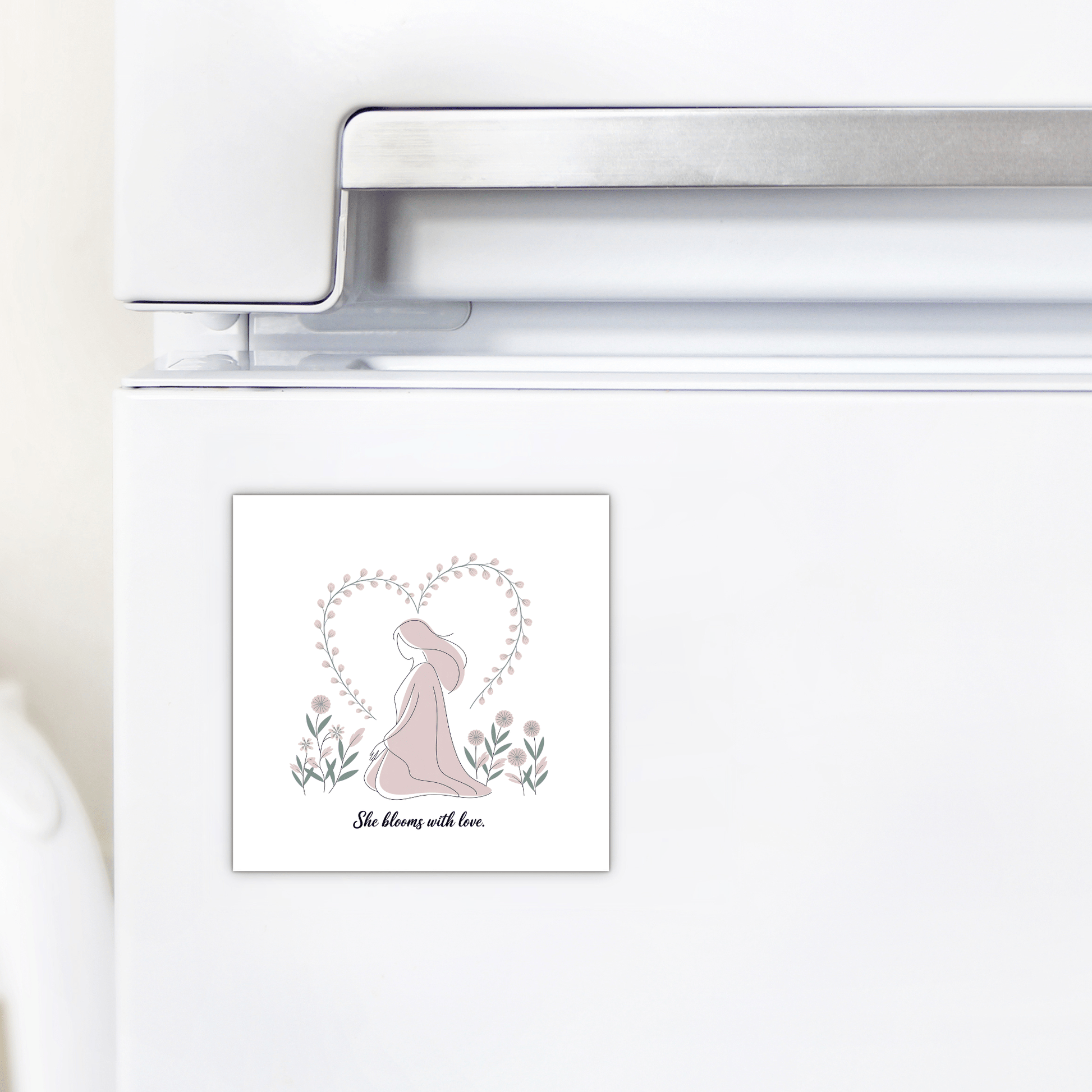 The Mirabilia Boutique She Blooms with Love Magnet – Gentle Floral Mom Gift, shown on a white fridge, depicts a woman in a hat within a heart of flowers and branches—an ideal decorative piece or special motherhood gift.