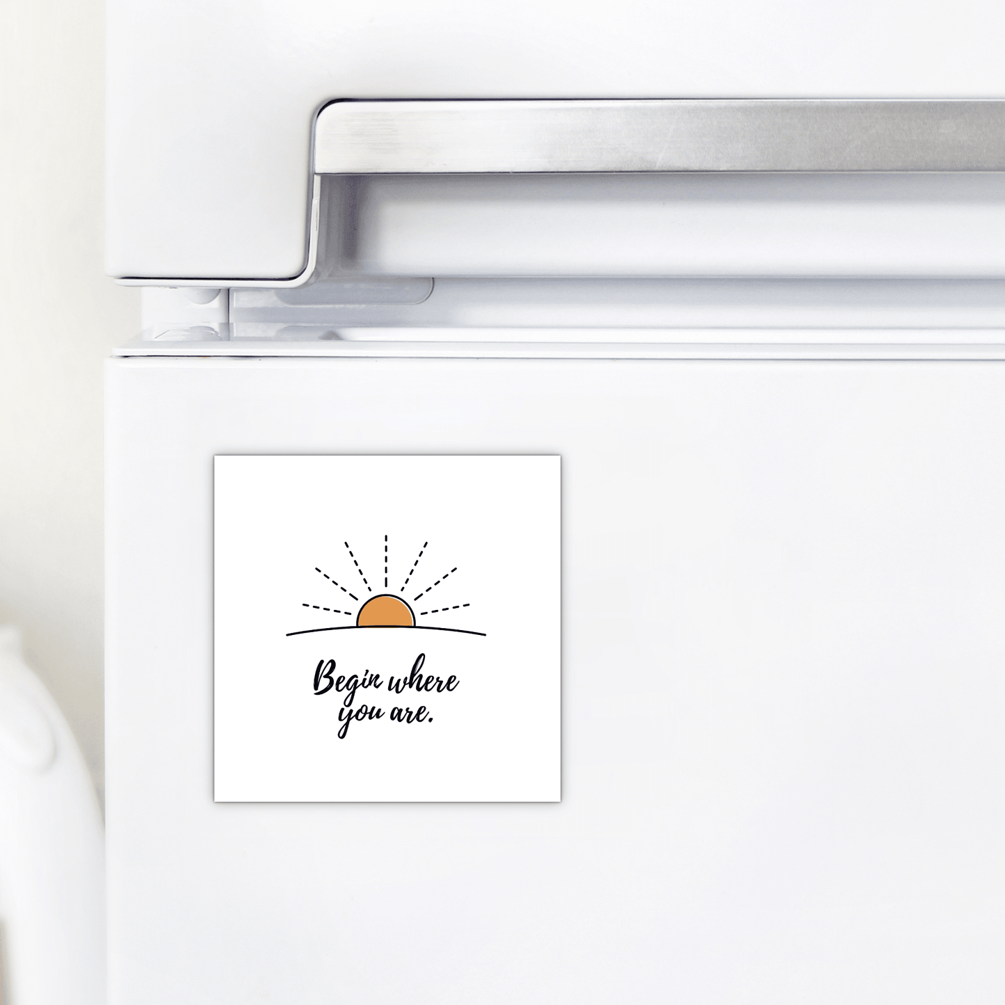 A white refrigerator displays the Mirabilia Boutique Begin Where You Are Magnet – Sunrise Affirmation, featuring a simple sunrise drawing and the phrase “Begin where you are.”.