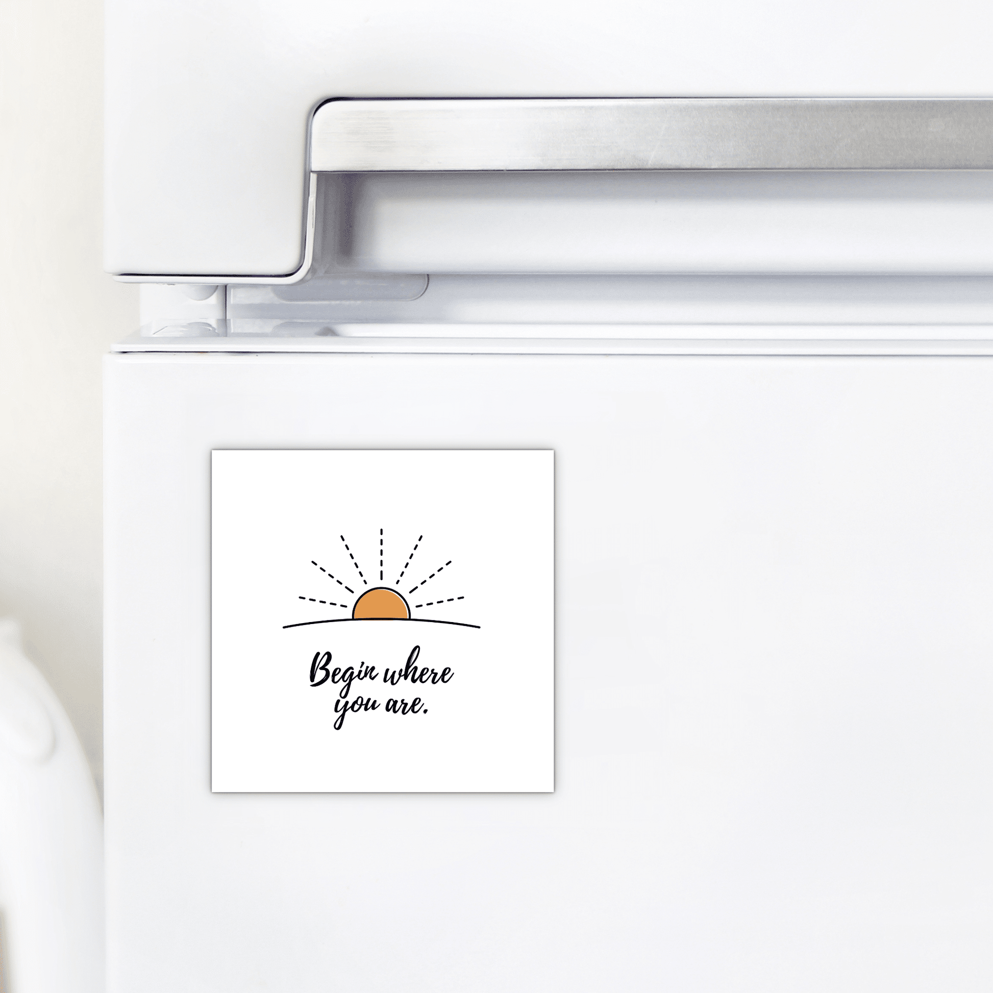 A white refrigerator displays the Mirabilia Boutique Begin Where You Are Magnet – Sunrise Affirmation, featuring a simple sunrise drawing and the phrase “Begin where you are.”.