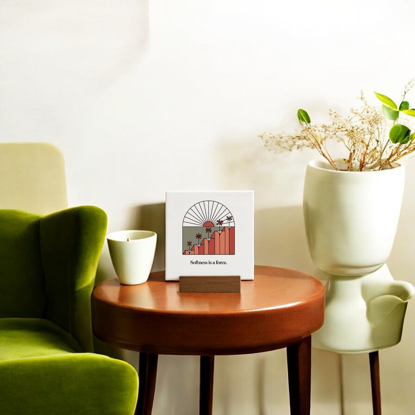 Create a cozy nook with Mirabilia Boutique’s "Softness Is a Force" Mini Canvas Sign, a green armchair, round wood table with a white cup, and a white planter of dried flowers—perfect minimalist decor for motivation.