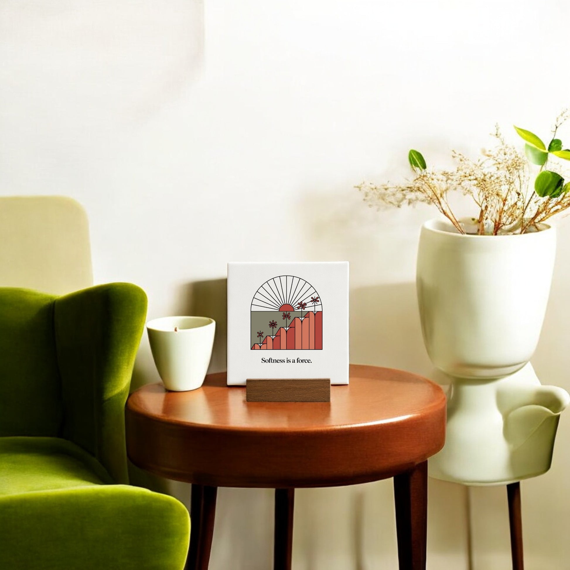Create a cozy nook with Mirabilia Boutique’s "Softness Is a Force" Mini Canvas Sign, a green armchair, round wood table with a white cup, and a white planter of dried flowers—perfect minimalist decor for motivation.