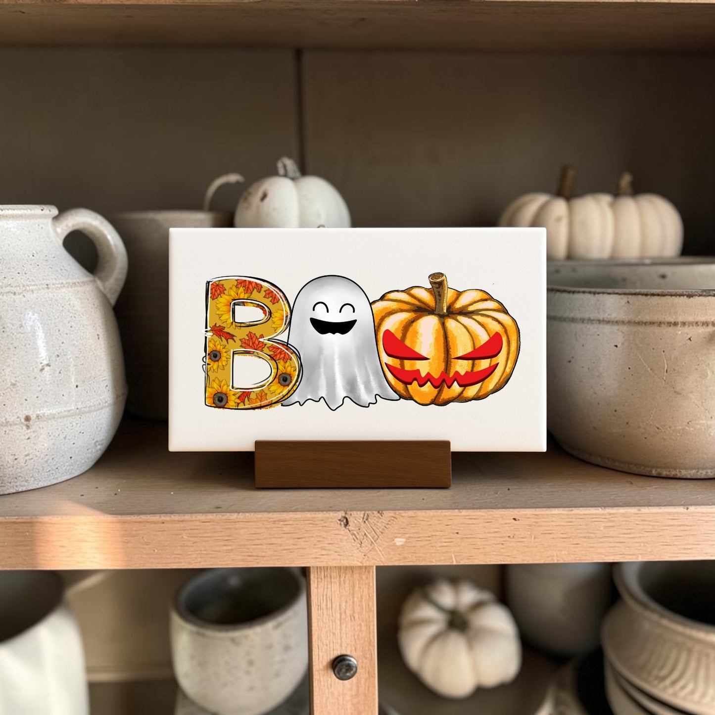 The BOO Ghost Pumpkin Mini Sign by Mirabilia Boutique features a floral "B," smiling ghost, and jack-o'-lantern—perfect Halloween shelf decor to pair with ceramic pots and white pumpkins.