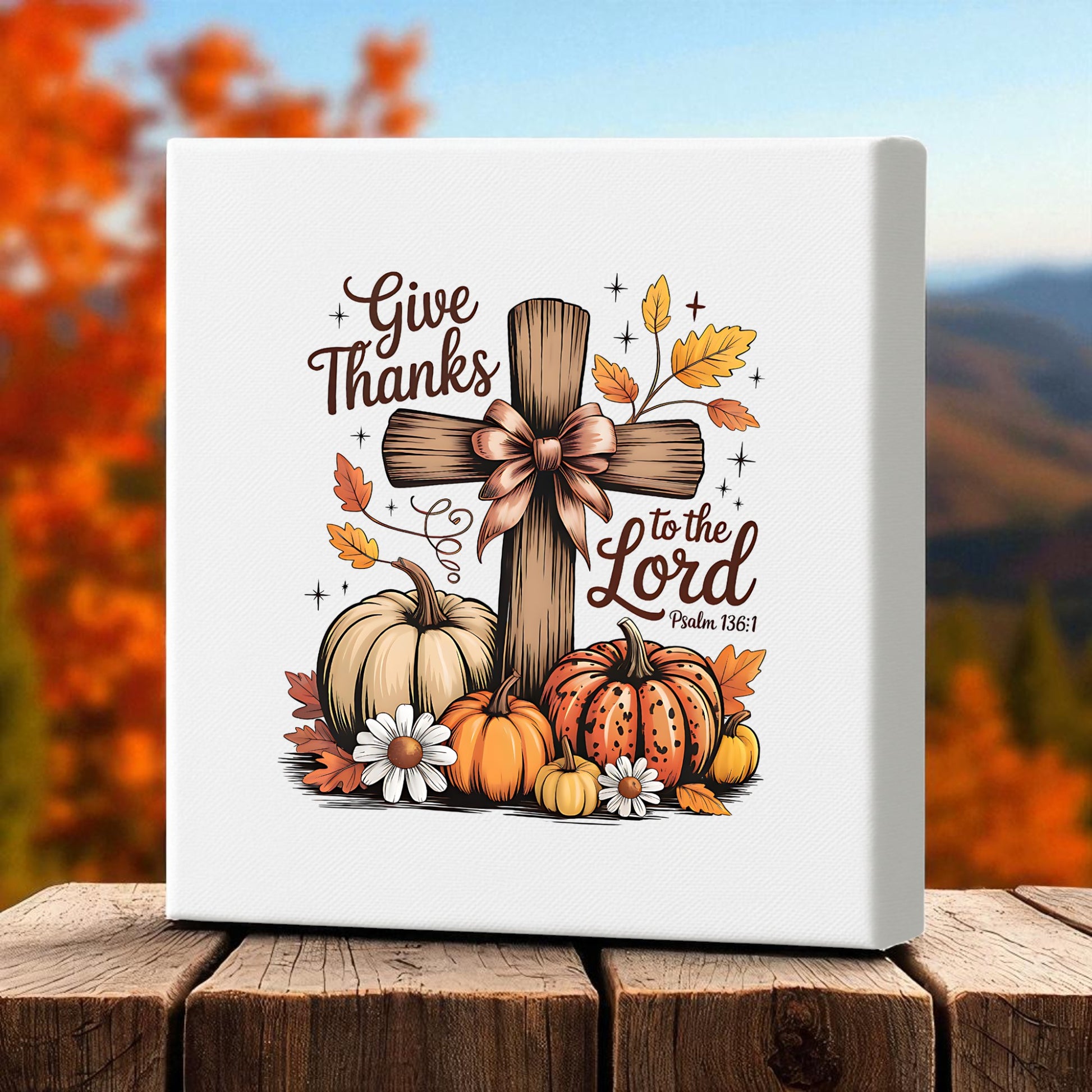 The Thanksgiving Canvas by Mirabilia Boutique features "Give thanks to the Lord" from Psalm 136:1, a rustic cross with a bow, pumpkins, leaves, and daisies—perfect fall décor for Thanksgiving.