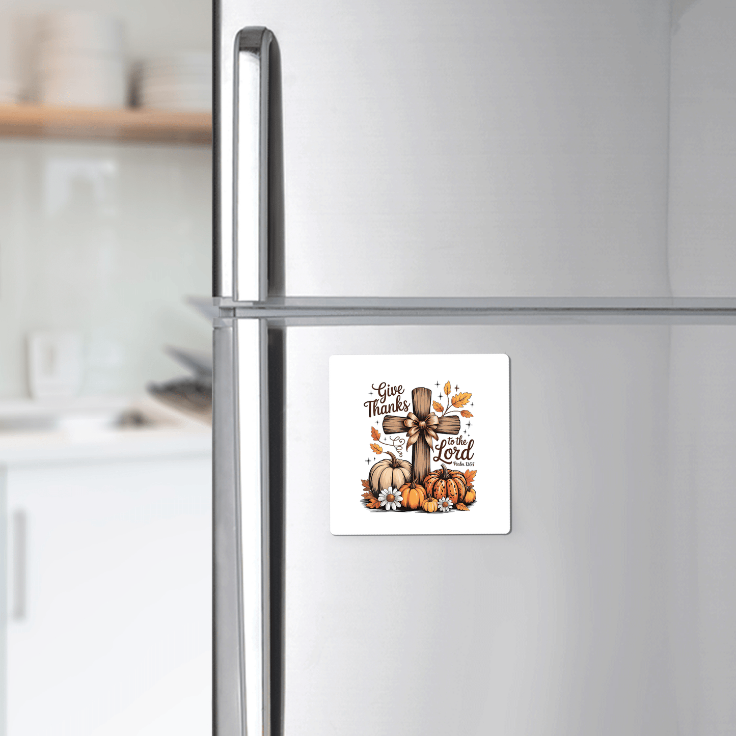 A silver fridge features the Mirabilia Boutique "Give Thanks Fall Magnet"—a square Christian magnet with pumpkins, sunflowers, leaves, a wooden cross, and “Give Thanks to the Lord" (Psalm 136:1)—perfect autumn décor or Thanksgiving gift. Kitchen shelves are in back.