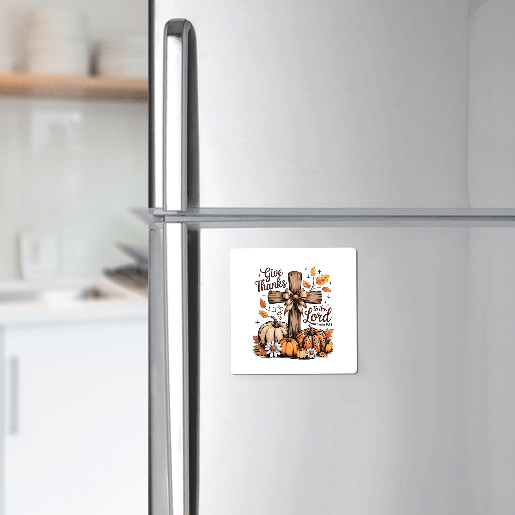A silver fridge features the Mirabilia Boutique "Give Thanks Fall Magnet"—a square Christian magnet with pumpkins, sunflowers, leaves, a wooden cross, and “Give Thanks to the Lord" (Psalm 136:1)—perfect autumn décor or Thanksgiving gift. Kitchen shelves are in back.