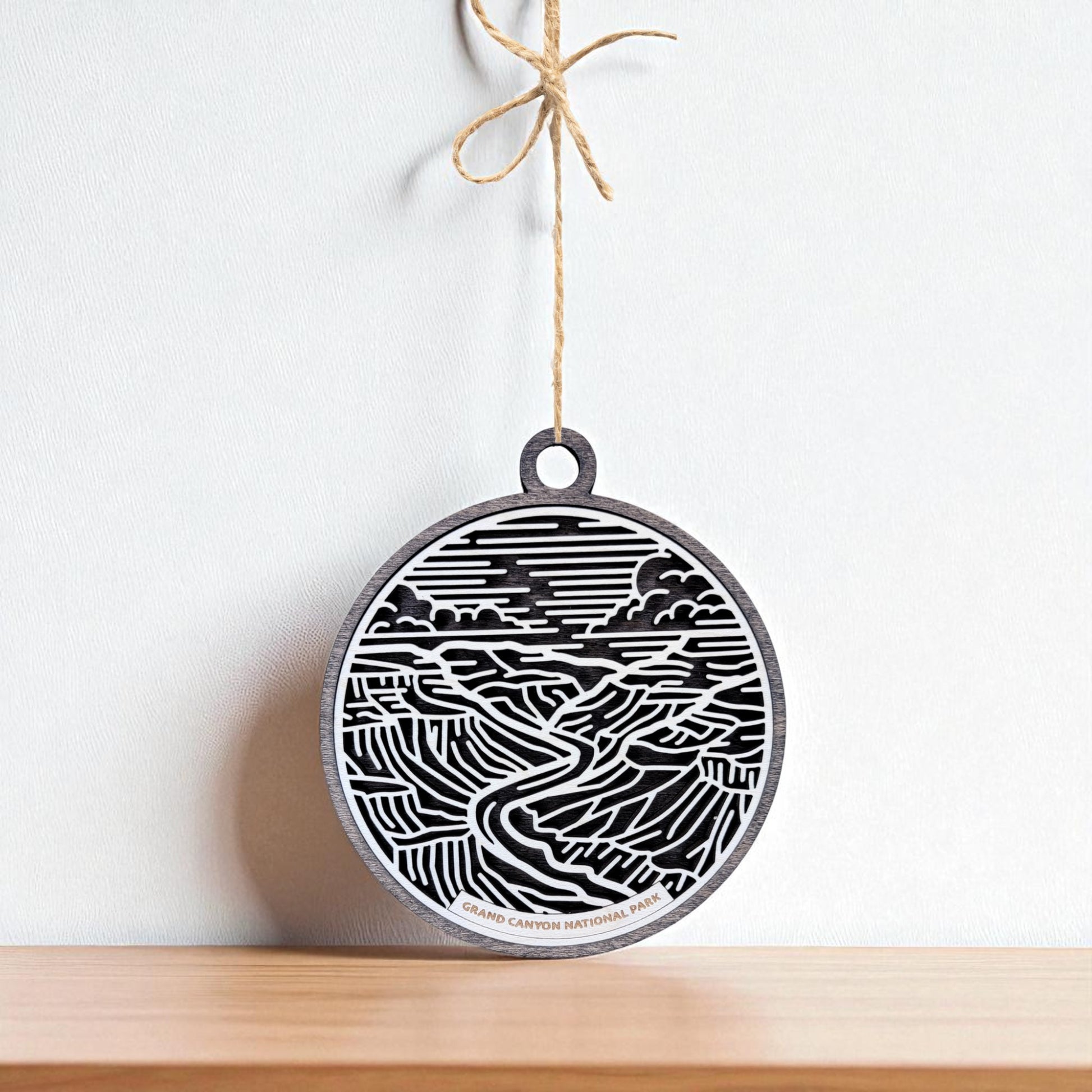 The Grand Canyon National Park Ornament by Mirabilia Boutique features detailed black and white line art, hanging elegantly from a string—perfect as a wooden travel gift for national park lovers.