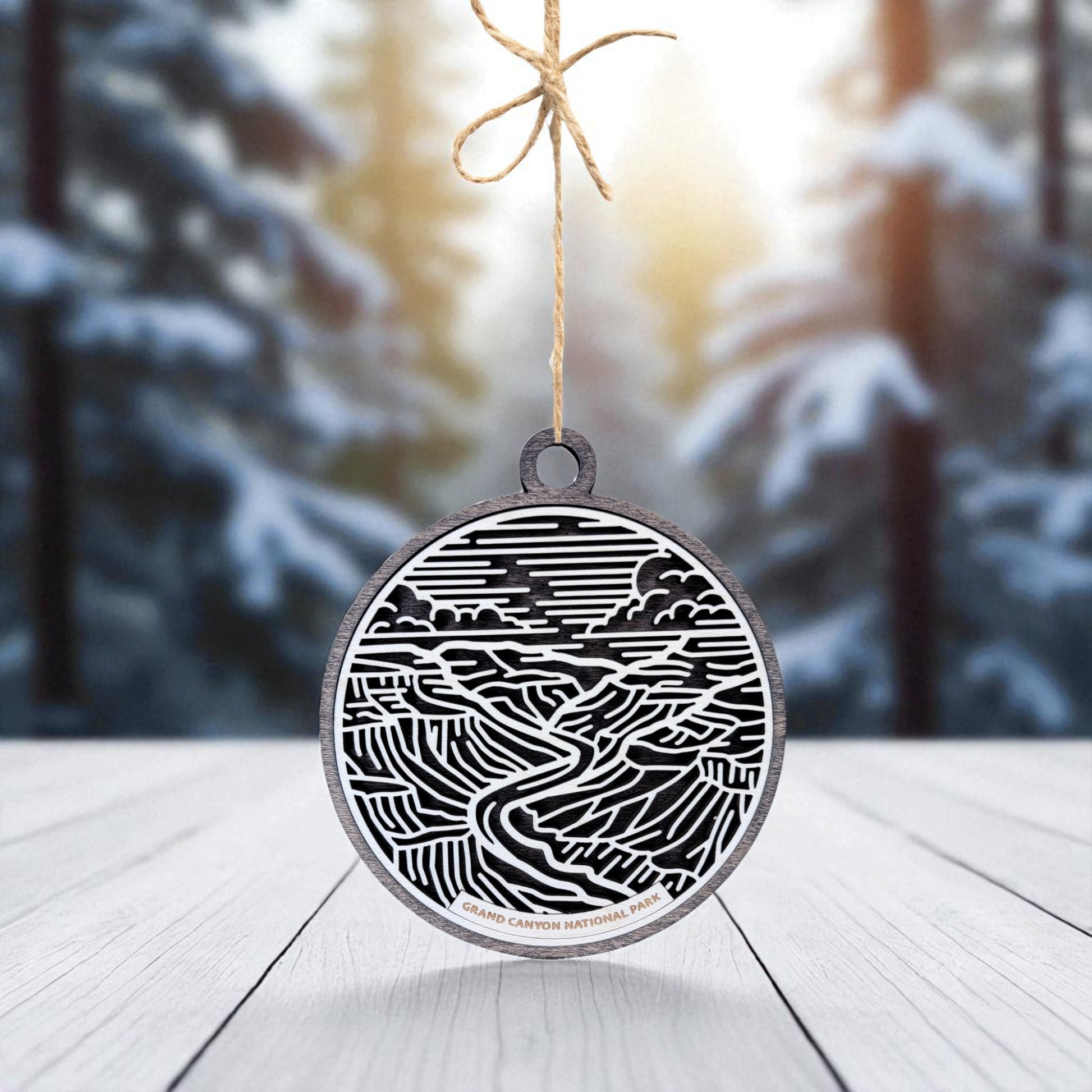 The Grand Canyon National Park Ornament by Mirabilia Boutique features a black and white design and hangs from a string. This wooden travel gift rests on a light wood surface—perfect for national park lovers.