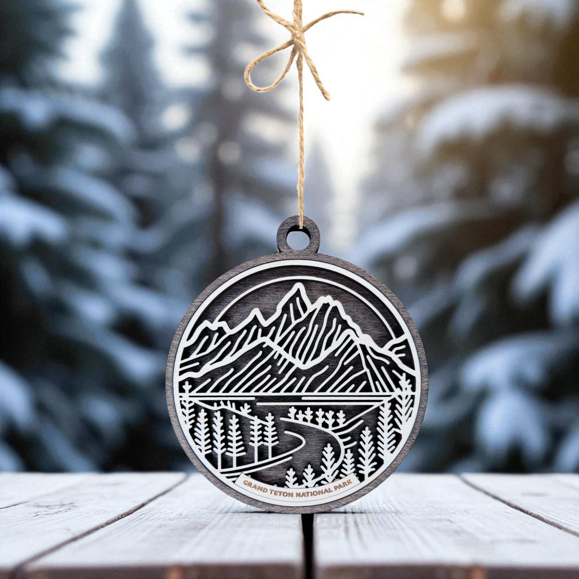 The Grand Teton National Park Ornament by Mirabilia Boutique features a wooden cutout of mountains, trees, and a river. Labeled with the park's name, this nature-inspired holiday decor makes a perfect mountain gift.