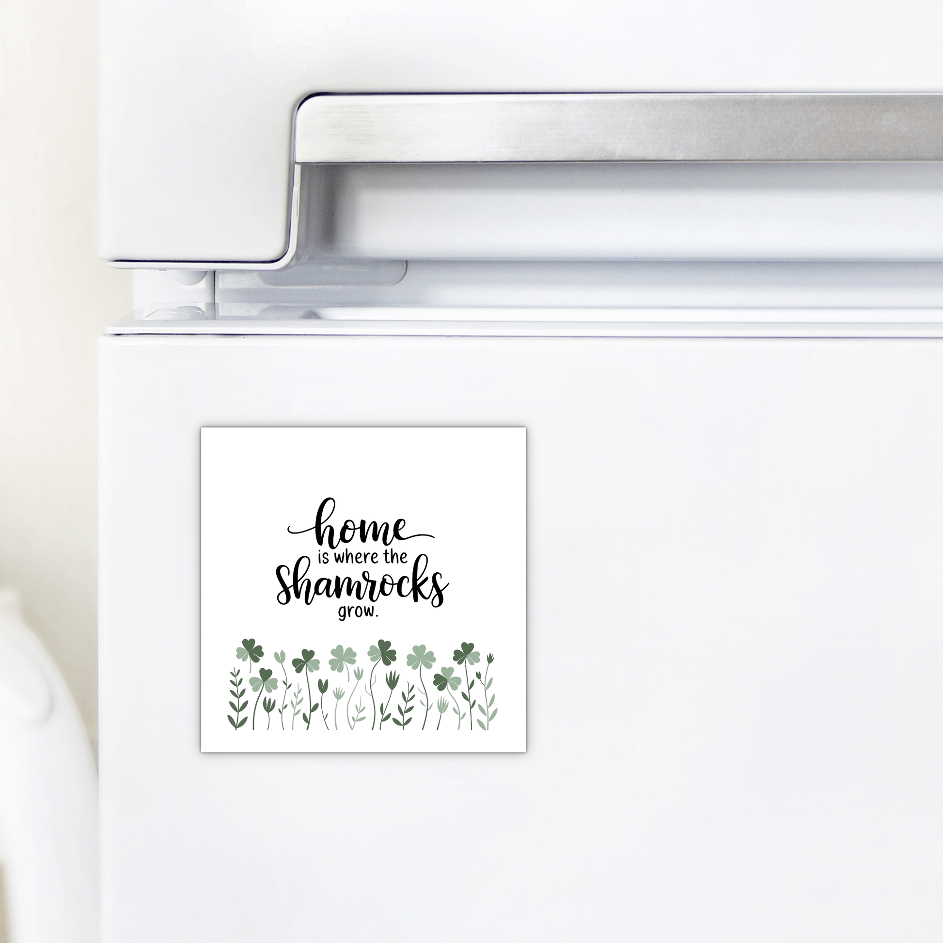 The Mirabilia Boutique "Home Is Where the Shamrocks Grow Magnet" adds a charming touch to any white refrigerator with its square design, green shamrocks, and leafy plants—perfect for Irish-inspired spring home decor.