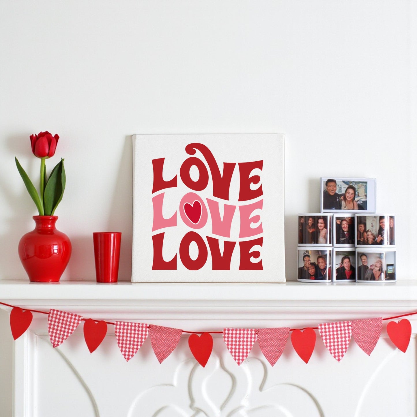 A white mantel with red accents—tulip vase, cup, heart garland, photo collage—features Mirabilia Boutique’s Retro LOVE Canvas in the center. This groovy Valentine decor reads "LOVE LOVE LOVE," ideal for romantic seasonal styling.