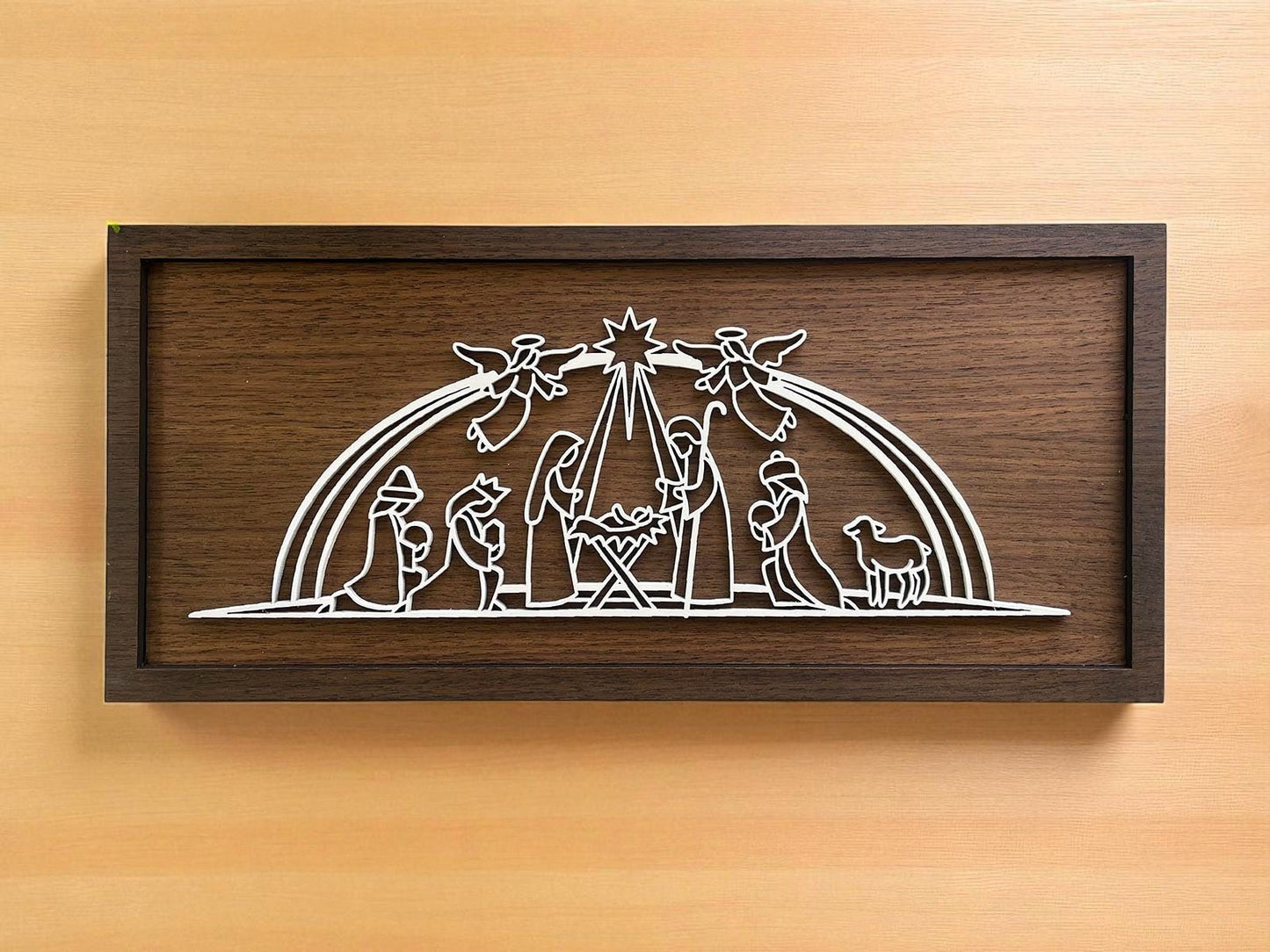The Large Nativity Scene Sign (18x8) by Mirabilia Boutique is a handmade laser-cut Christmas decor featuring Mary, Joseph, baby Jesus, shepherds, angels, and a sheep in white on a rustic wood background beneath a star.