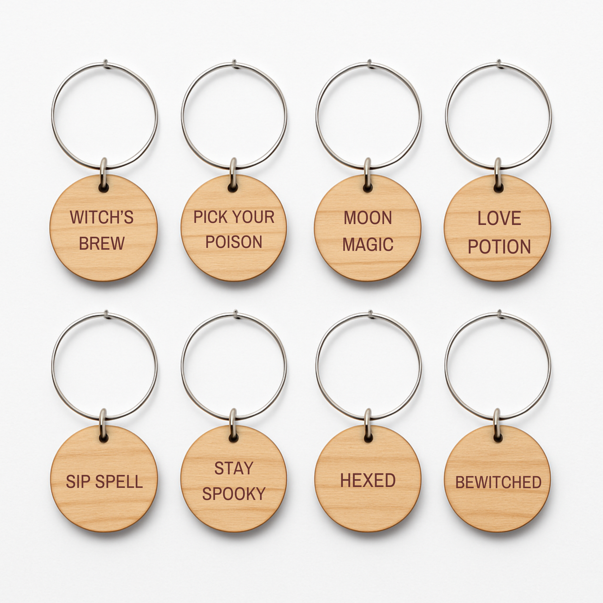 The Haunted Harvest Rustic Wine Charms Set by Mirabilia Boutique includes eight wooden keychains with round tags, each laser-engraved with a unique witchy phrase—WITCH'S BREW, PICK YOUR POISON, MOON MAGIC, LOVE POTION, SIP SPELL, STAY SPOOKY, HEXED, and BEWITCHED. Perfect for using as spooky wine glass markers or Halloween wine charms at your next magically rustic gathering.
