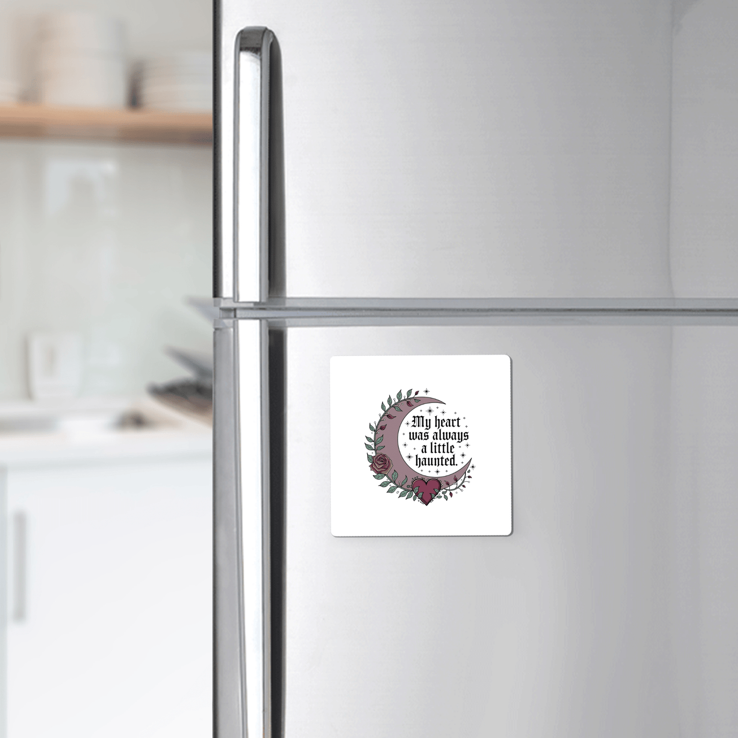 A silver refrigerator displays the Mirabilia Boutique Gothic Fridge Magnet—Haunted Heart Crescent Moon Design. A white kitchen is visible in the background.