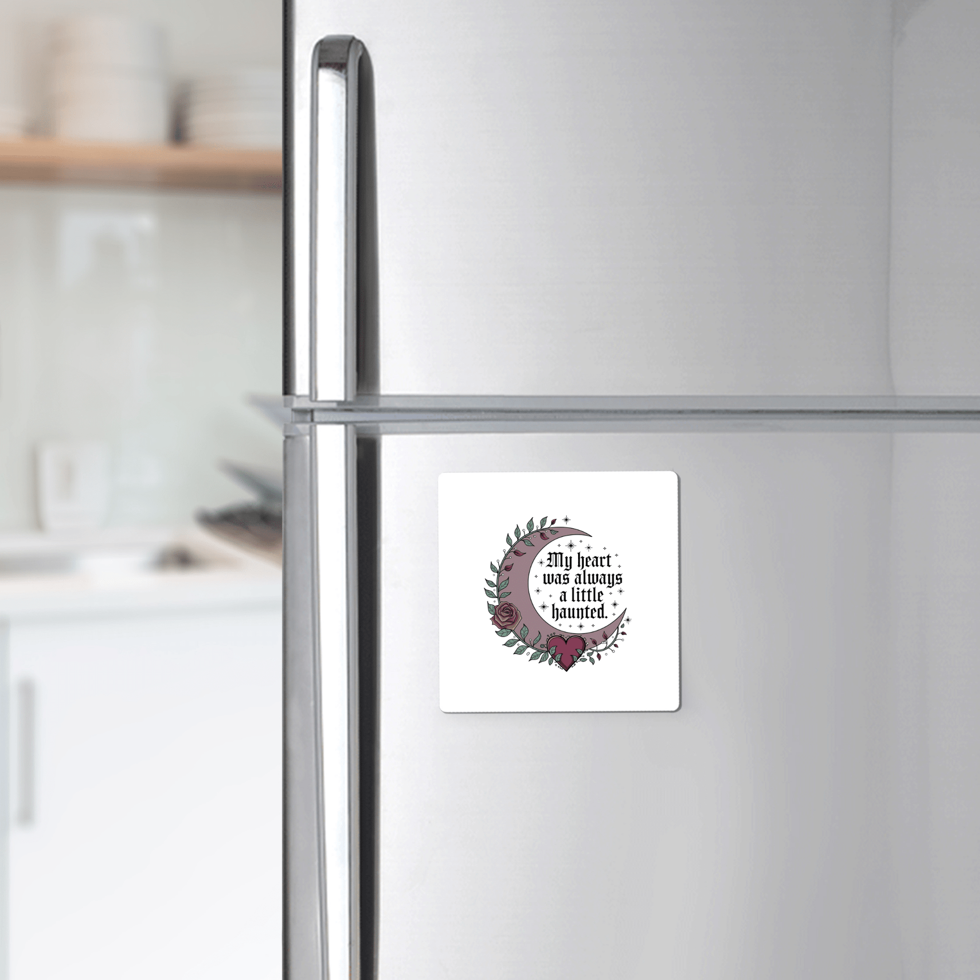 A silver refrigerator displays the Mirabilia Boutique Gothic Fridge Magnet—Haunted Heart Crescent Moon Design. A white kitchen is visible in the background.