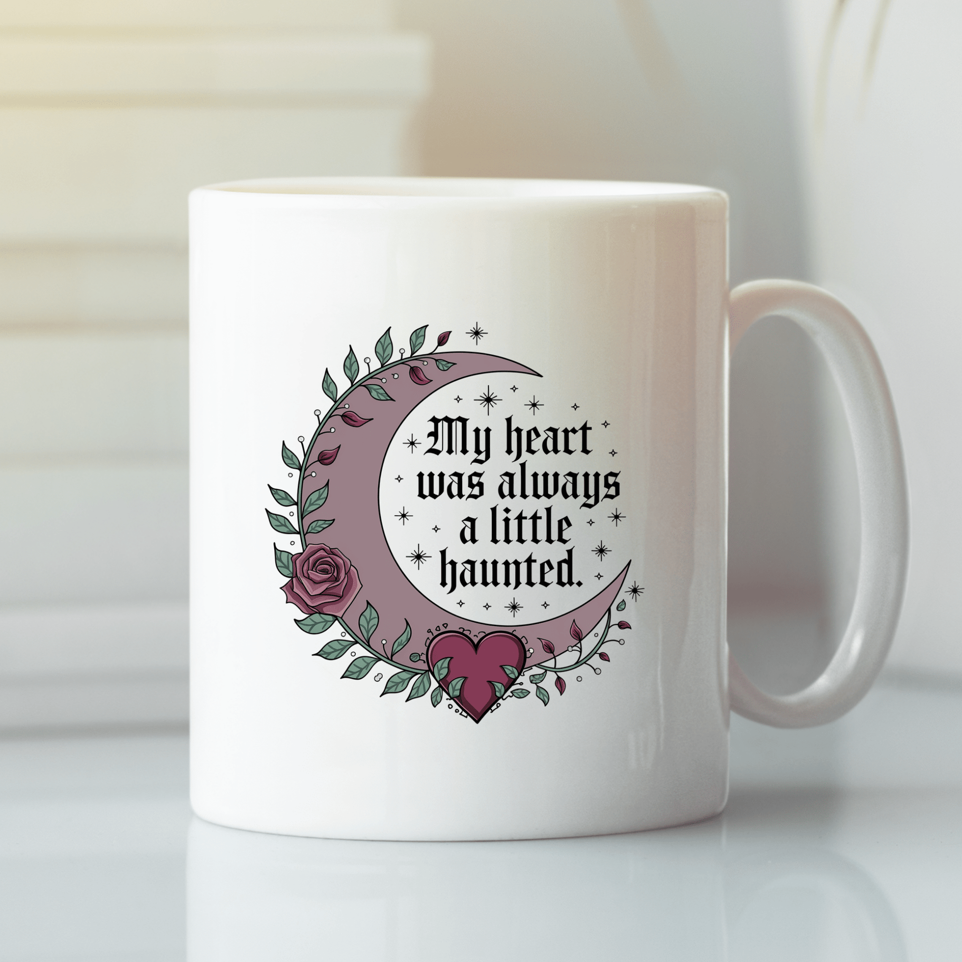 The Mirabilia Boutique Gothic Mug features white ceramic, a crescent moon, leaves, a rose, and a heart with "My Heart Was Always a Little Haunted" in gothic font.