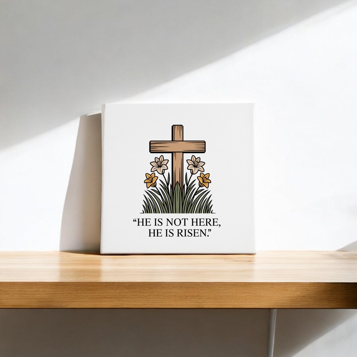 The He Is Risen Cross & Lily Canvas – 8x8 Easter Art from Mirabilia Boutique features a wooden cross, lilies, and green grass with the message "HE IS NOT HERE, HE IS RISEN." It’s perfect as Easter decor for your shelf or wall.