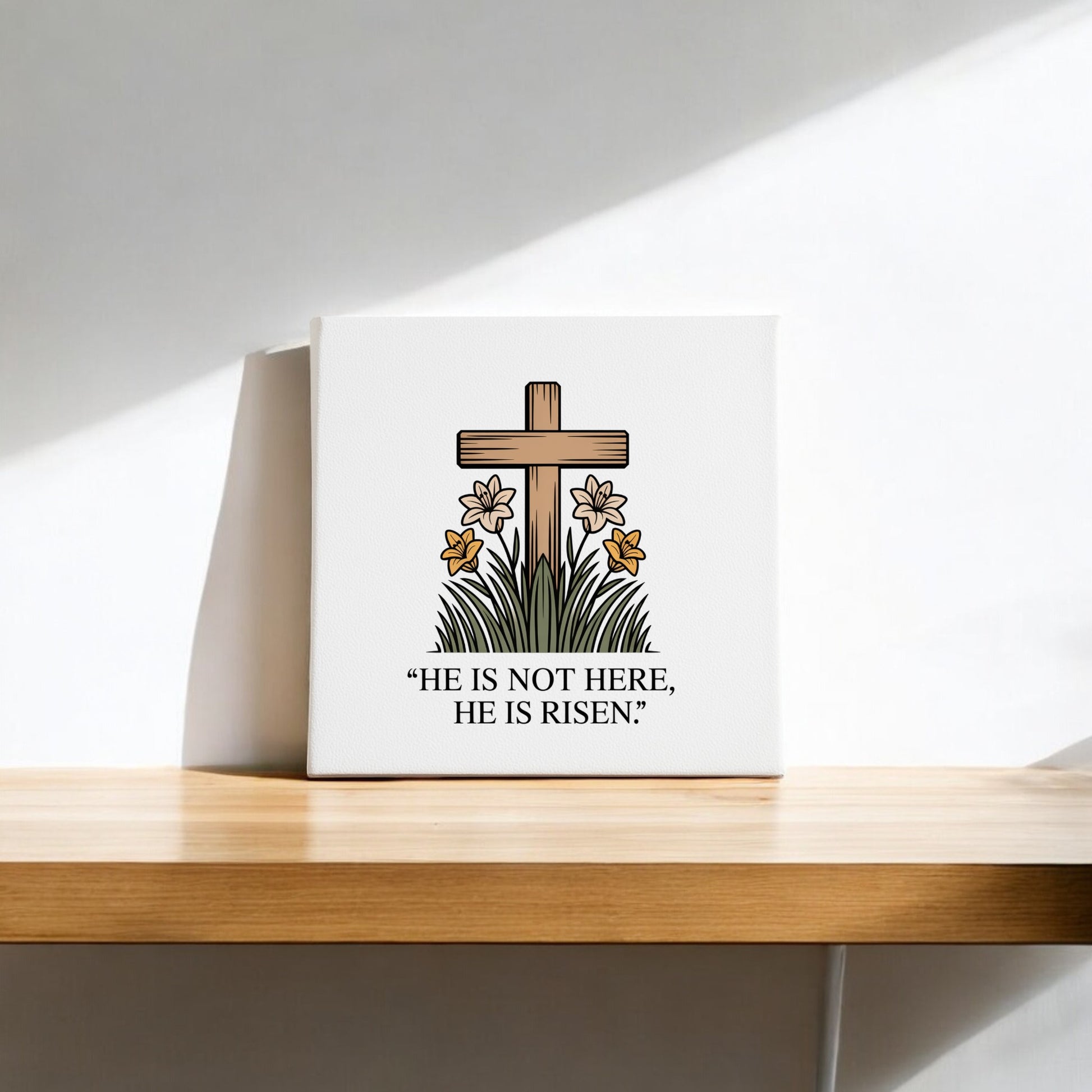 The He Is Risen Cross & Lily Canvas – 8x8 Easter Art from Mirabilia Boutique features a wooden cross, lilies, and green grass with the message "HE IS NOT HERE, HE IS RISEN." It’s perfect as Easter decor for your shelf or wall.